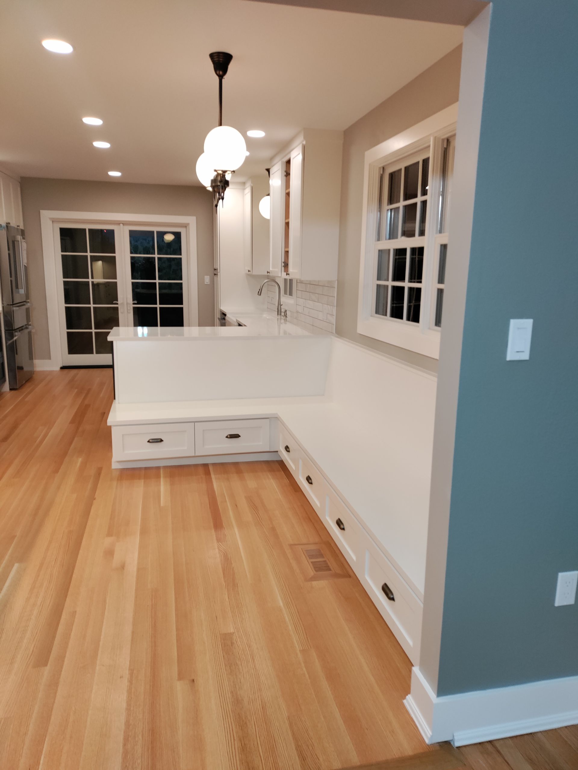 Empty modern kitchen with white cabinets, wood floors, and pendant lights