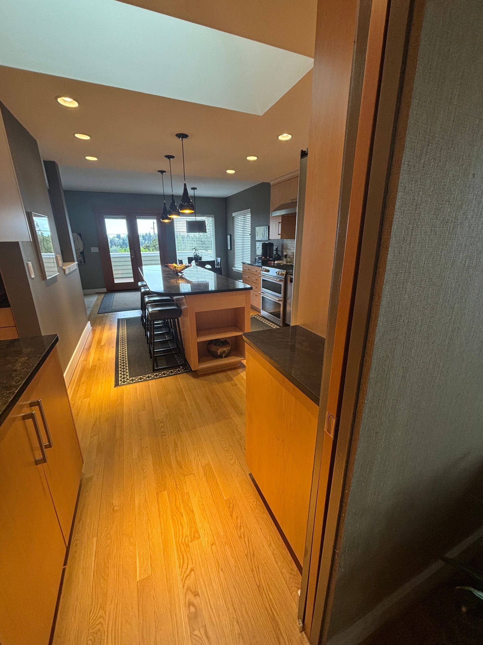 Kitchen hallway leading to a modern dining area with wood floors, pendant lights, and a central island