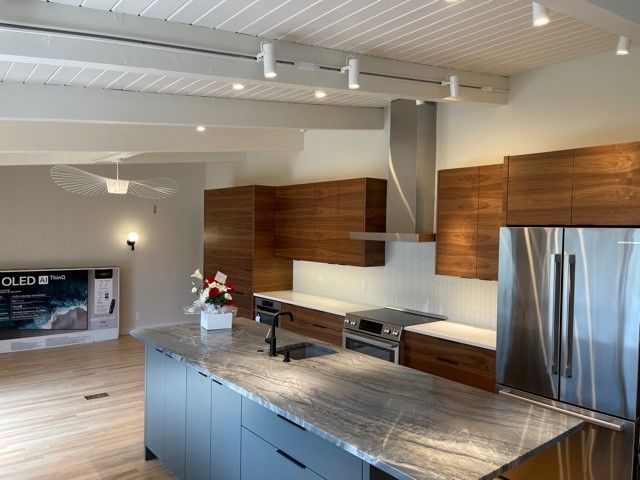Modern kitchen with island, stainless steel fridge, wood cabinets, and open living area