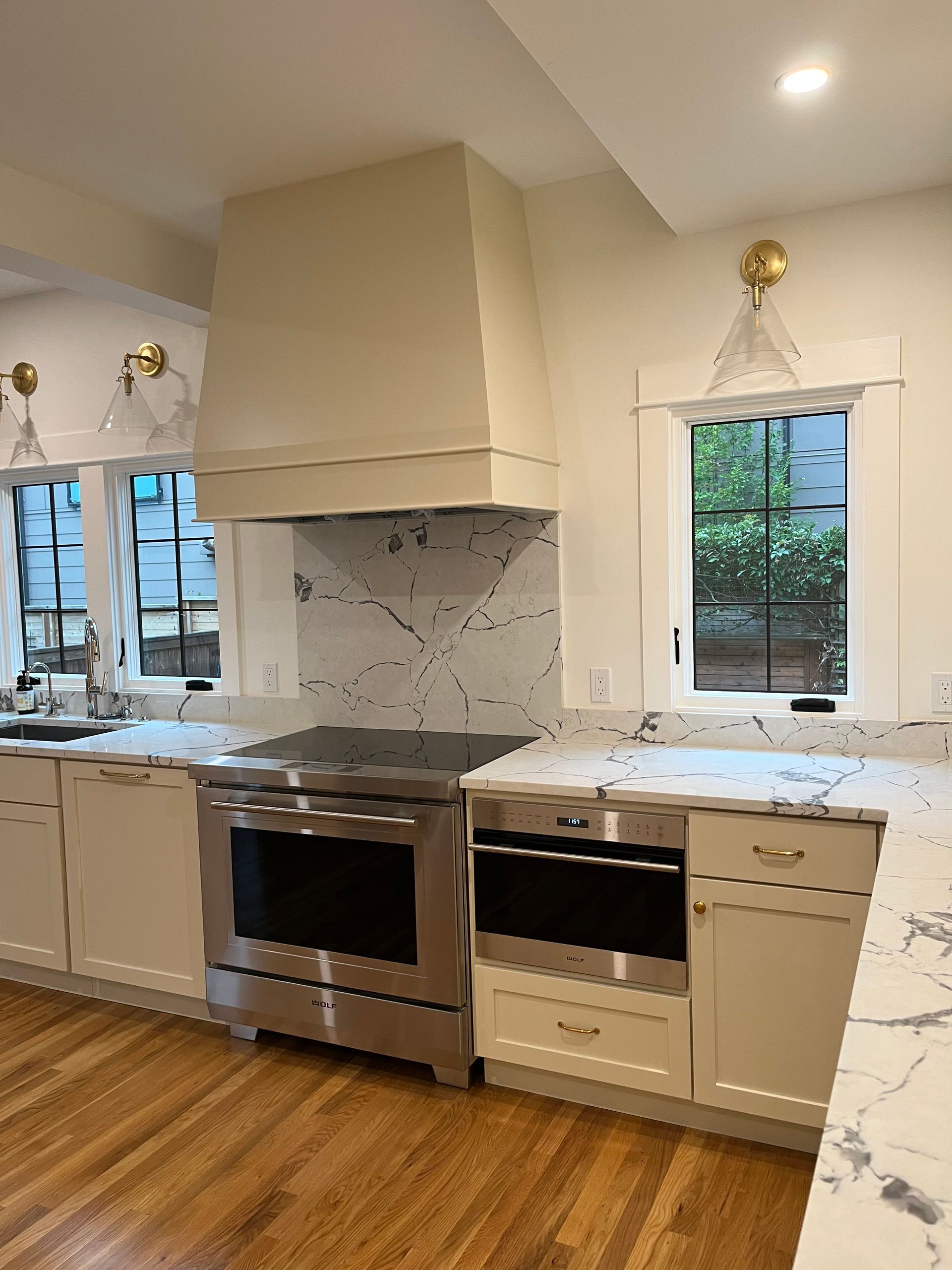 Modern kitchen with white cabinets, marble backsplash, stainless stove, and wood floors under a window