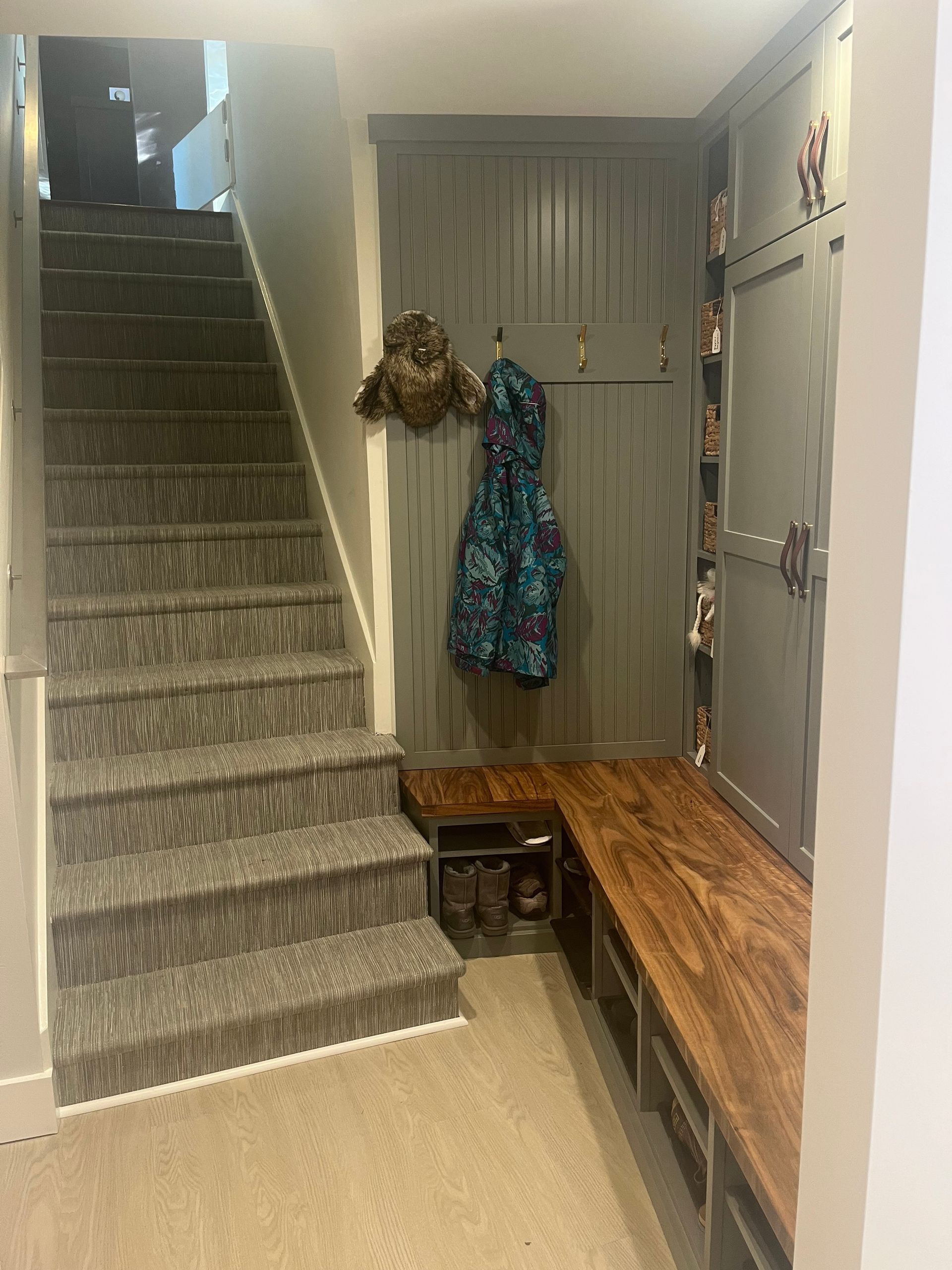 Narrow entryway with carpeted stairs, a wooden bench, and coats hanging by a door.