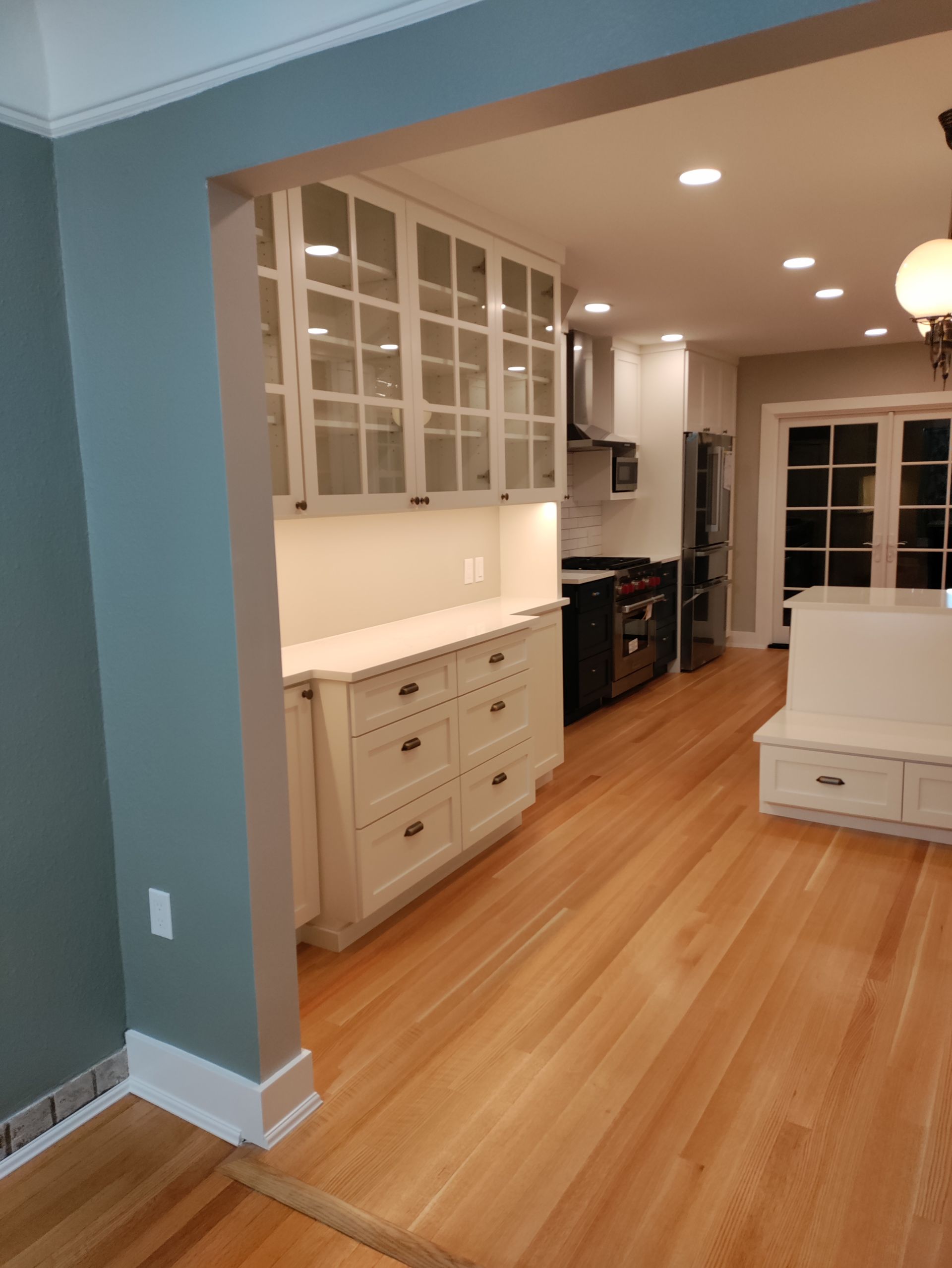 Bright kitchen with wood floors, white cabinets, and a dining nook with a bench near large windows