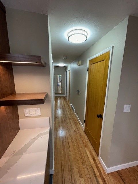 Narrow hallway with wood floors, white walls, ceiling light, built-in shelves, and a closed wooden door