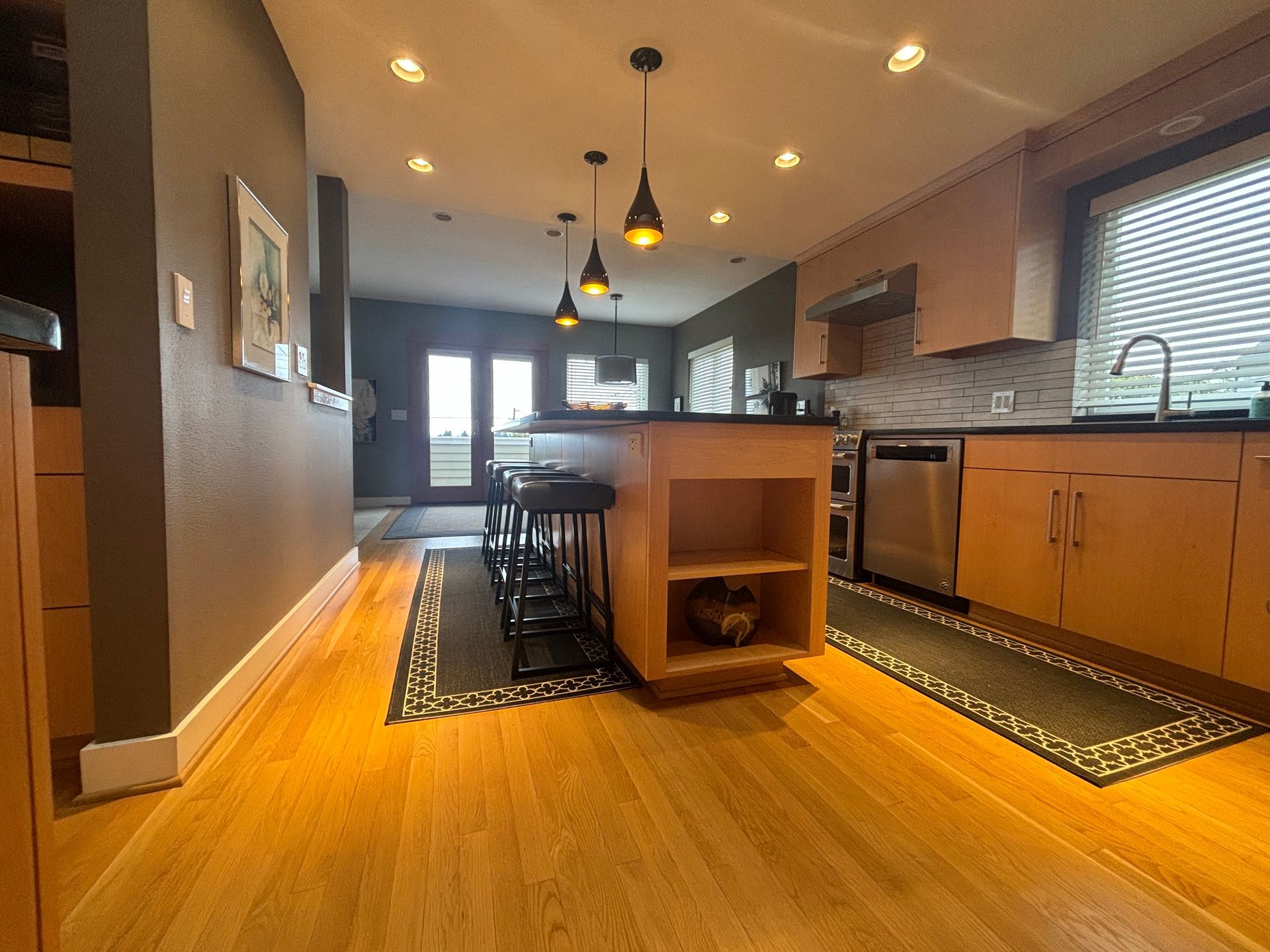 Modern kitchen and dining area with wood floors, island, pendant lights, and stainless appliances