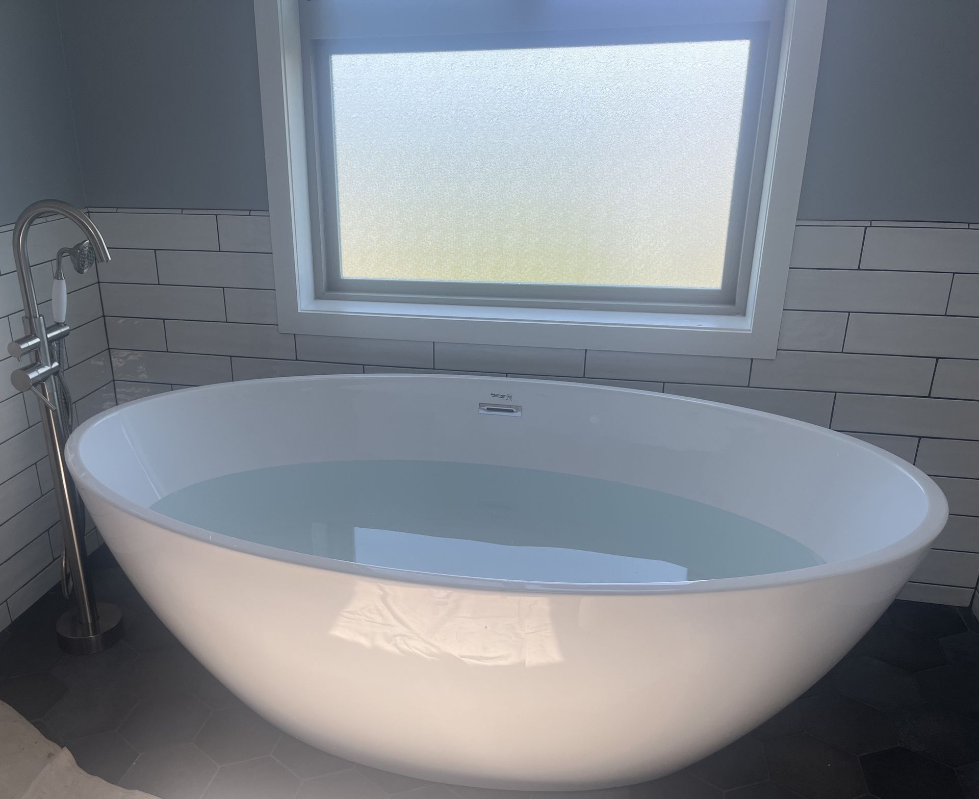 Modern bathroom with a freestanding white oval bathtub beneath a frosted window