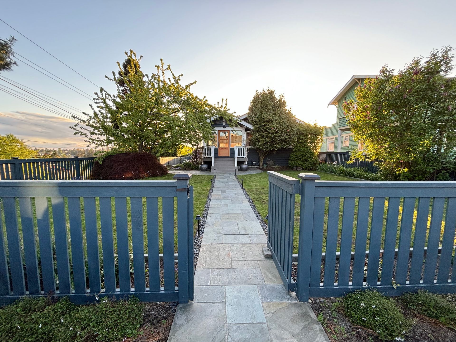 Blue gate opening to a stone path leading to a house in a sunlit garden