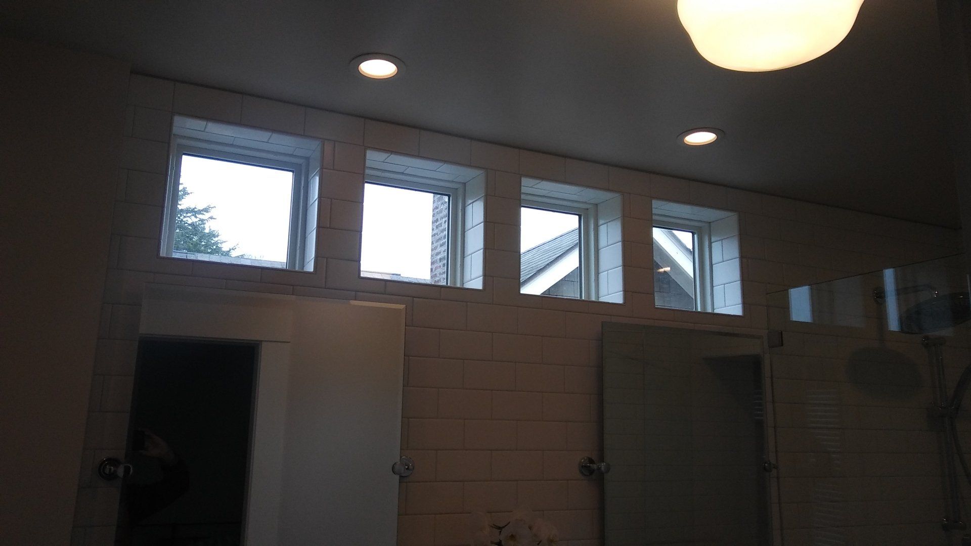 Dim restroom interior with tiled walls, small high windows, and ceiling lights