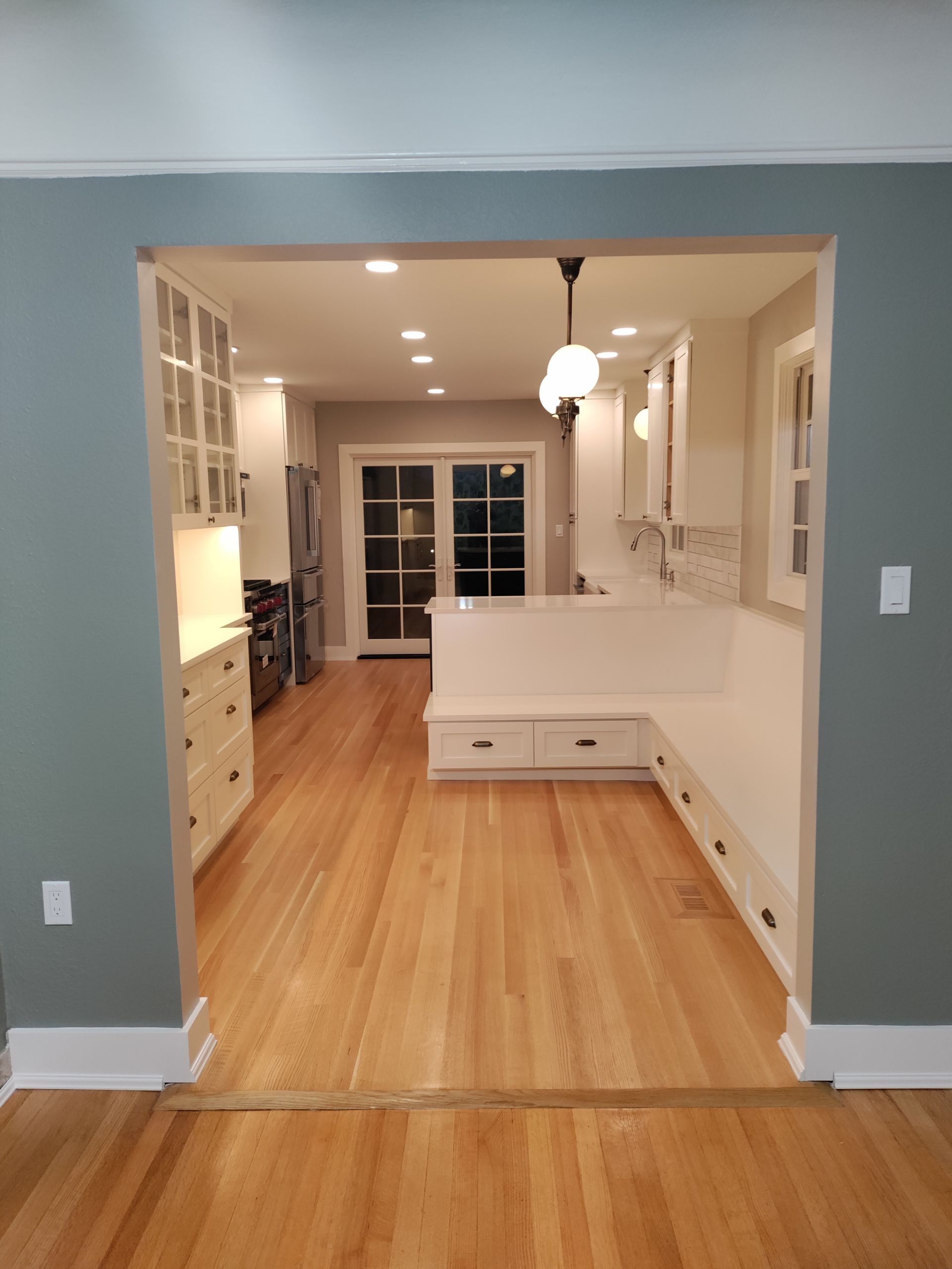 Open-concept dining area with light wood floors, white cabinets, and a glass door at the far end.