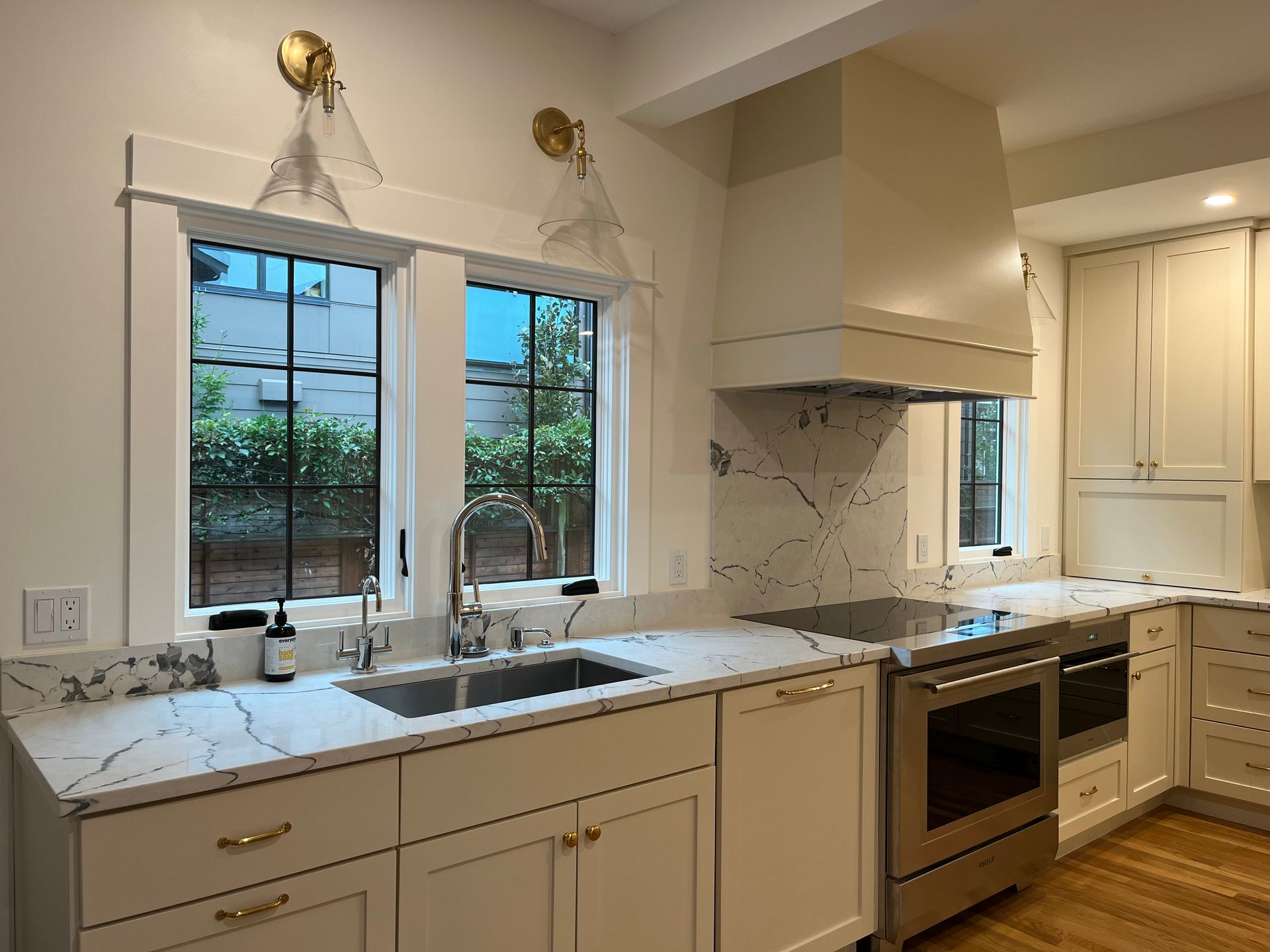 Bright kitchen with white cabinets, marble countertops, double sink, and large windows over the sink.