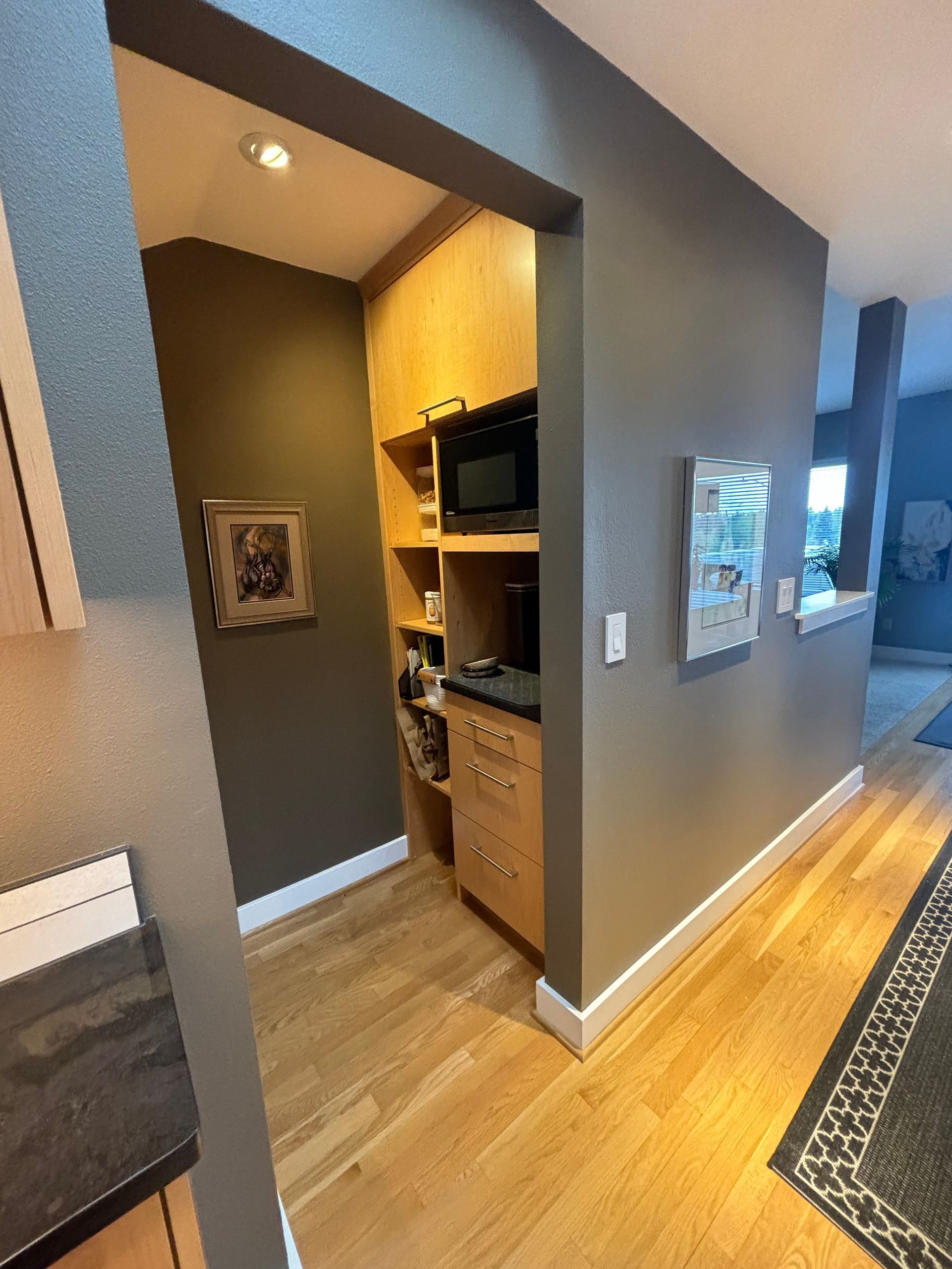 Hallway with hardwood floors, gray walls, and a kitchen nook with cabinets, microwave, and framed art.
