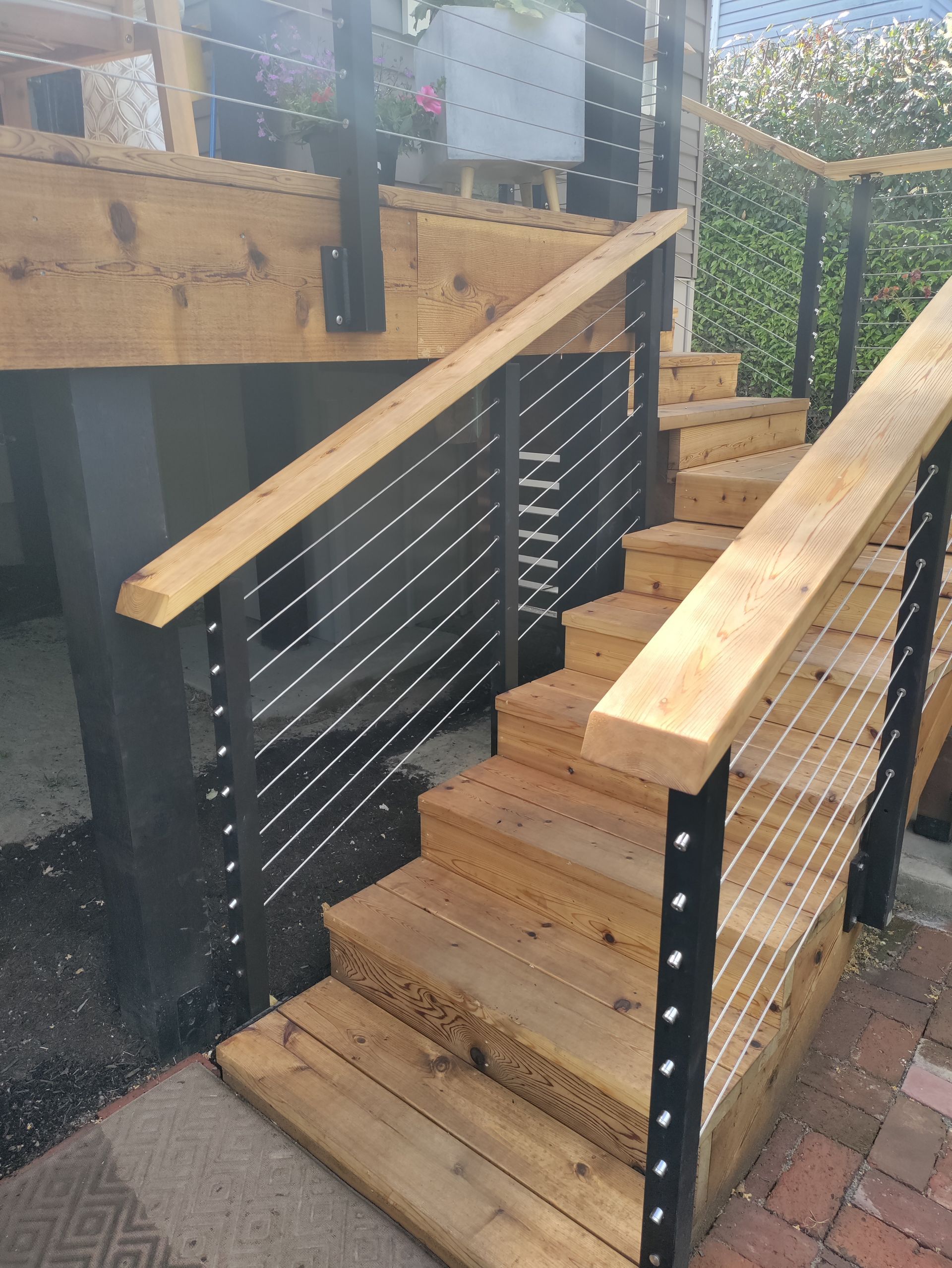 Wooden outdoor accessibility ramp with black railings and steps leading to a raised deck