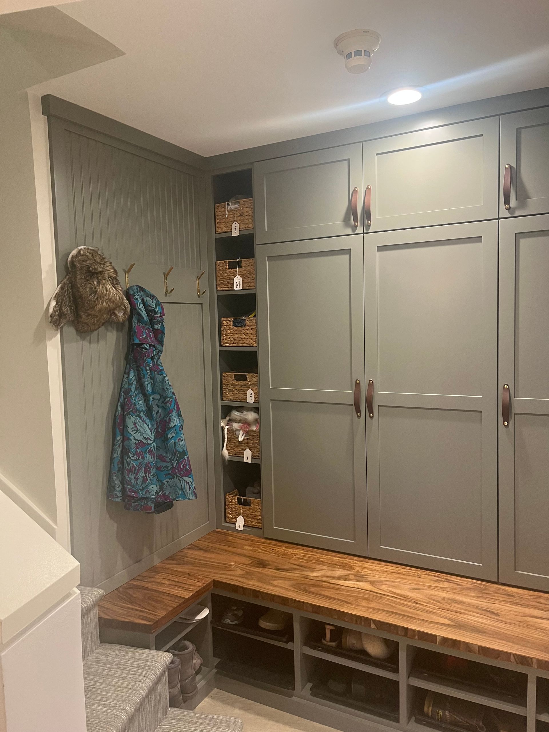 Entryway mudroom with built-in gray cabinets, bench seating, and a coat hanging on the wall.