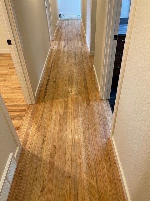 Narrow hallway with light wood floors and white walls, viewed toward a brighter room at the end.