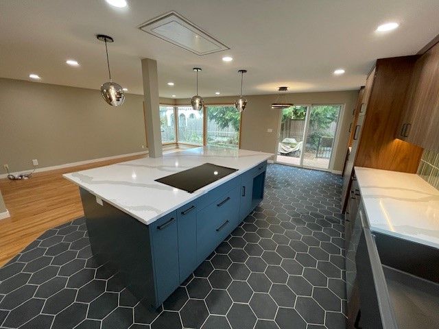 Modern kitchen with blue island, hex tile floor, wood accents, and large windows overlooking greenery