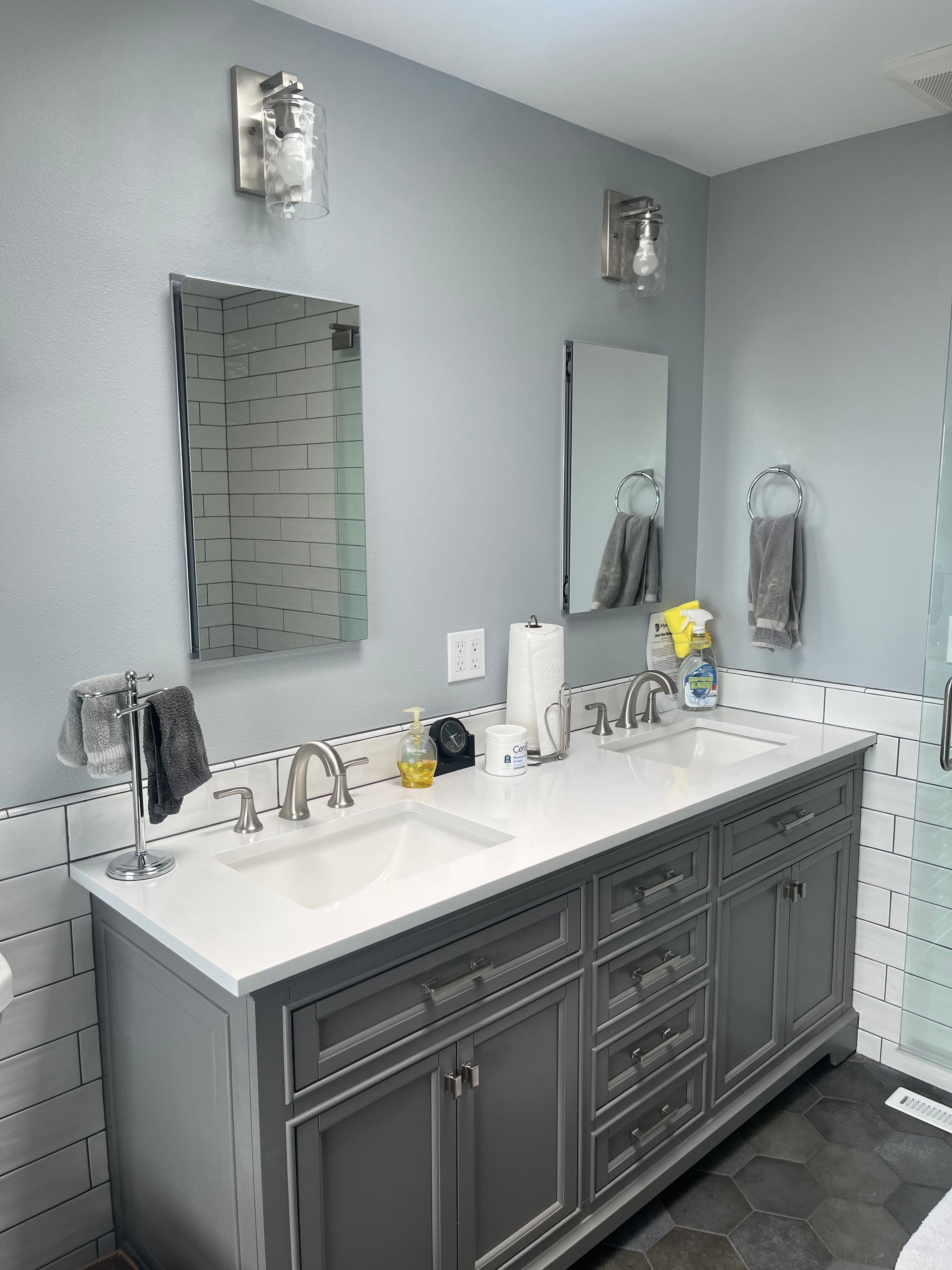 Gray bathroom with double vanity, two mirrors, and white countertop with sink and toiletries