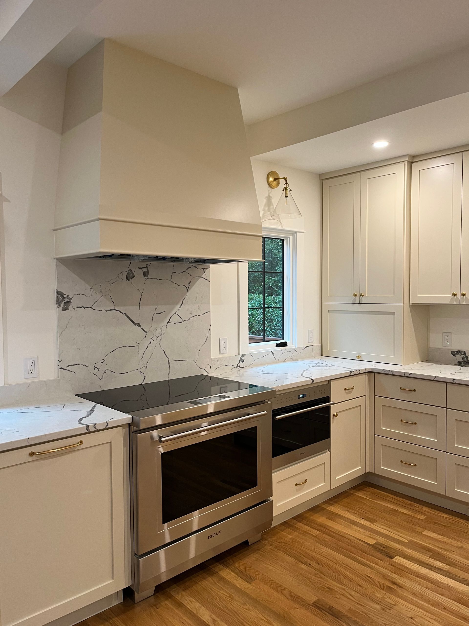 Modern kitchen with white cabinets, stainless steel range, marble backsplash, and wood floors