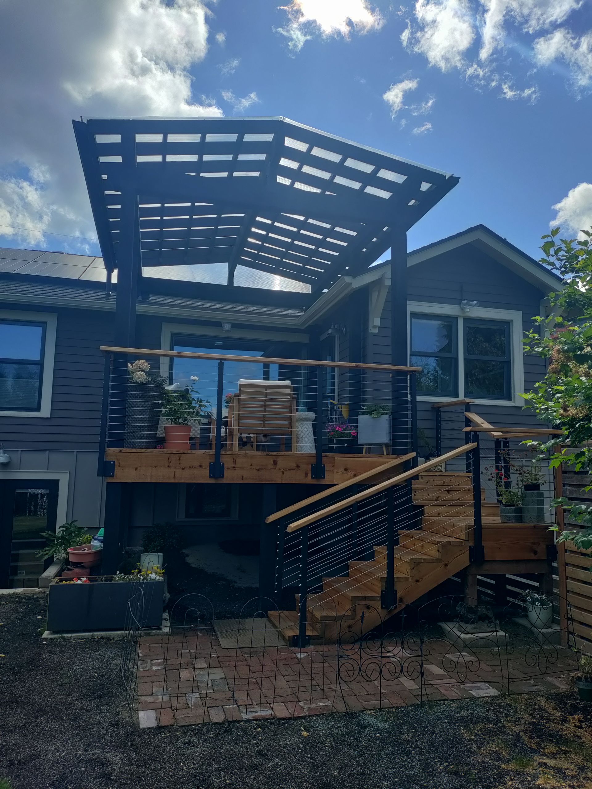 Modern house deck with pergola roof, blue siding, and brick stairs in a backyard garden