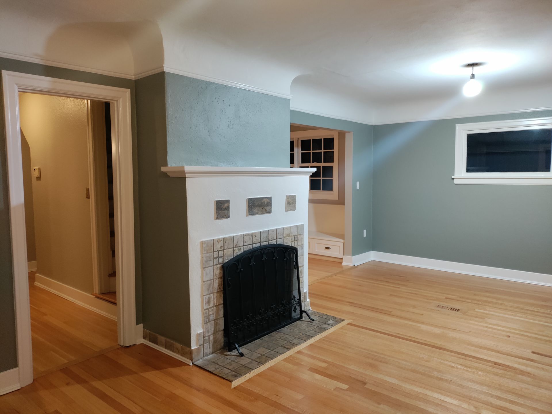 Empty living room with white brick fireplace, hardwood floors, and blue-gray walls