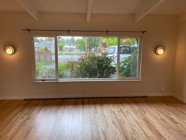 Empty living room with hardwood floors, large window, and wall sconces looking out onto greenery