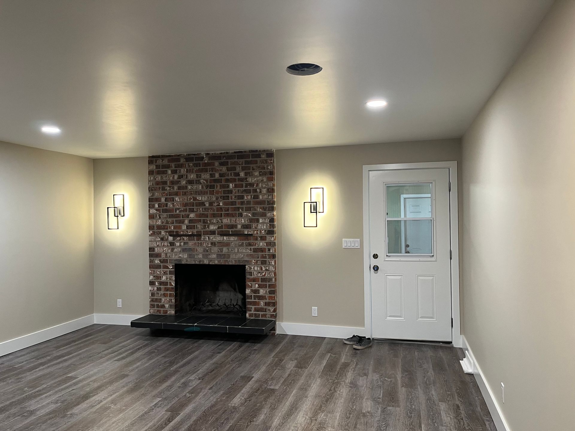 Empty living room with brick fireplace, wall sconces, and white door on the right.