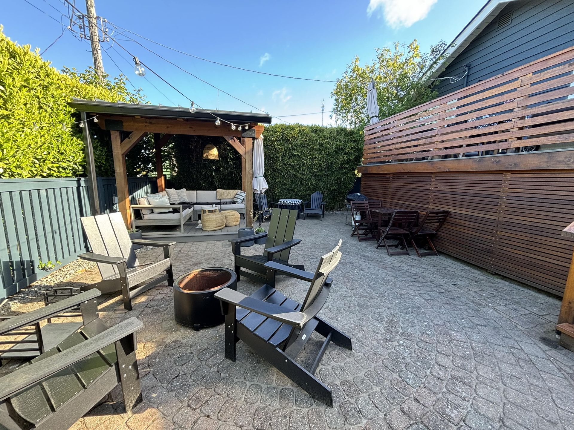 Backyard patio with fire pit, Adirondack chairs, gazebo, and gravel ground under a blue sky