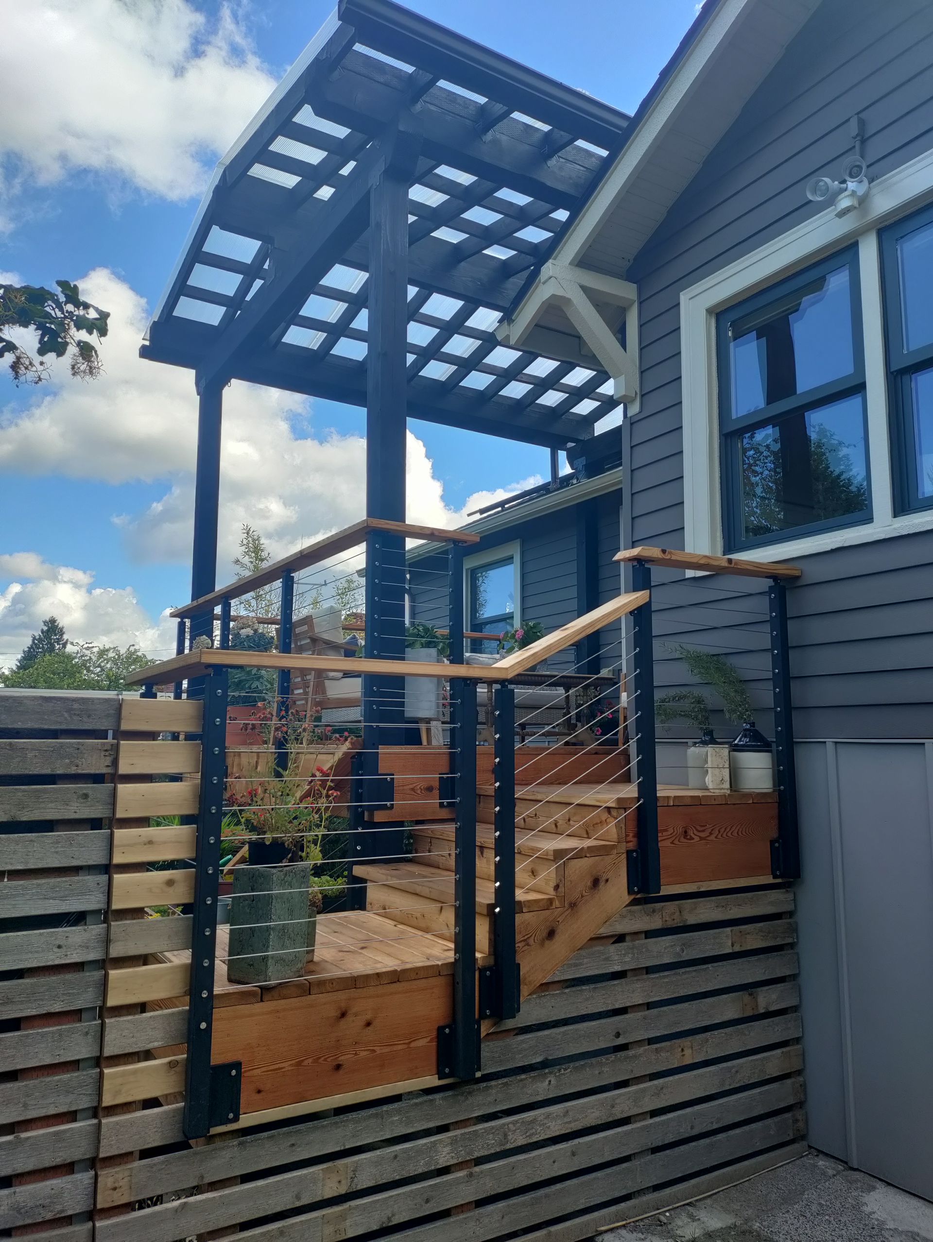 Modern house exterior with wooden slat fence, glass gate, and pergola under a blue sky