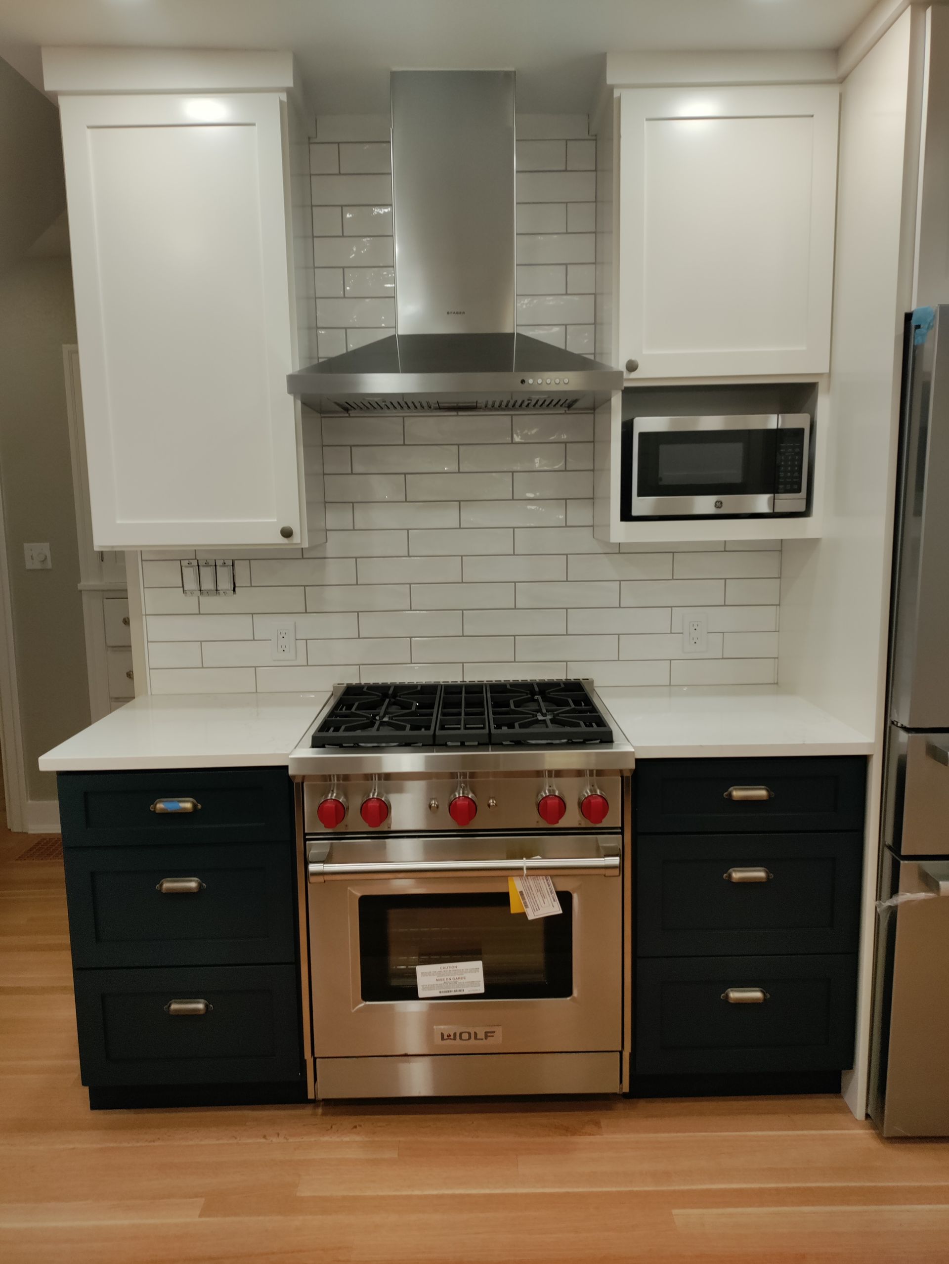 Modern kitchen with white cabinets, stainless range and hood, black drawers, and built-in microwave