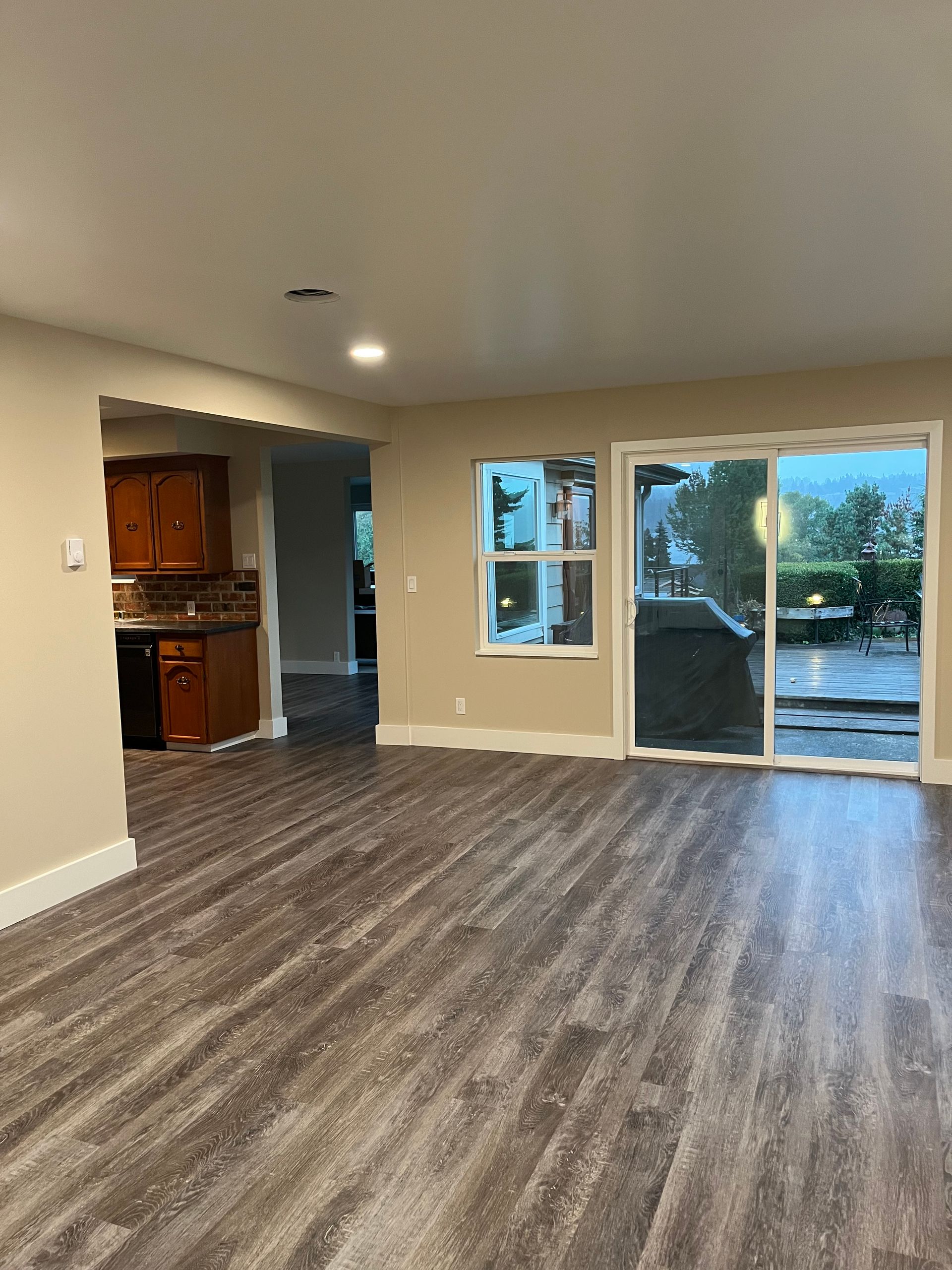 Empty living room with wood-look floors, beige walls, and sliding glass doors to a patio.