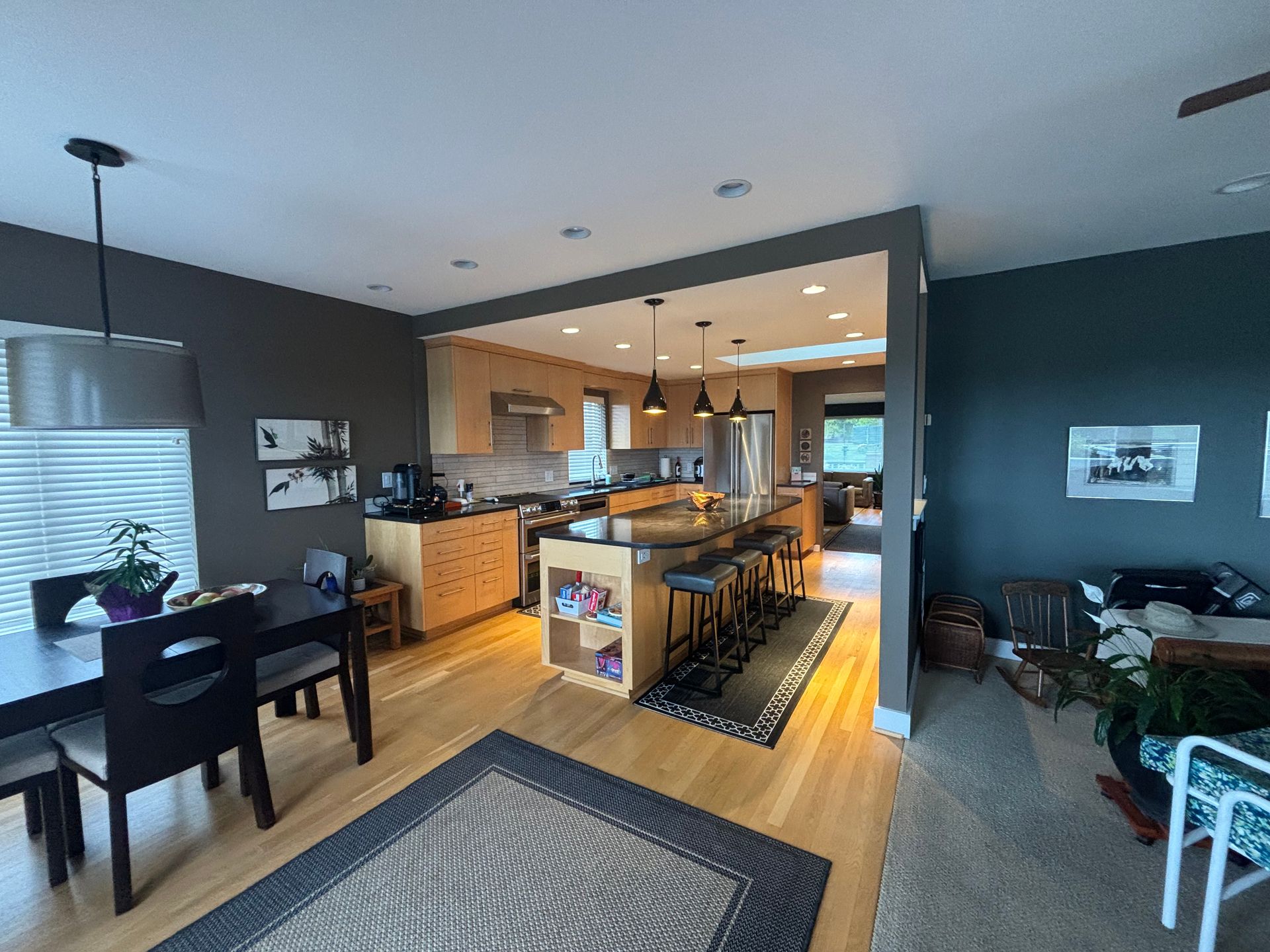 Open-plan kitchen and dining area with wood floors, dark walls, and a patterned rug