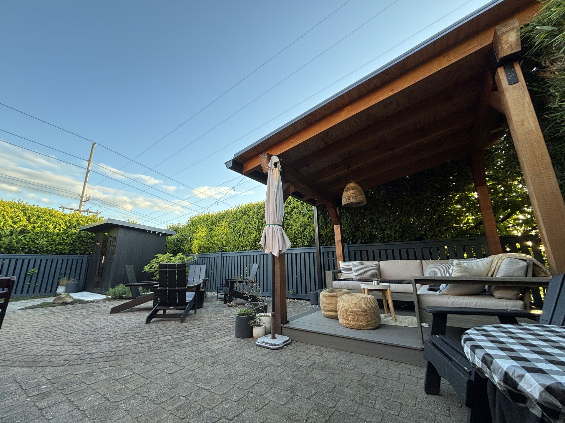 Outdoor patio with wooden gazebo, seating, umbrella, and gravel yard under a blue sky