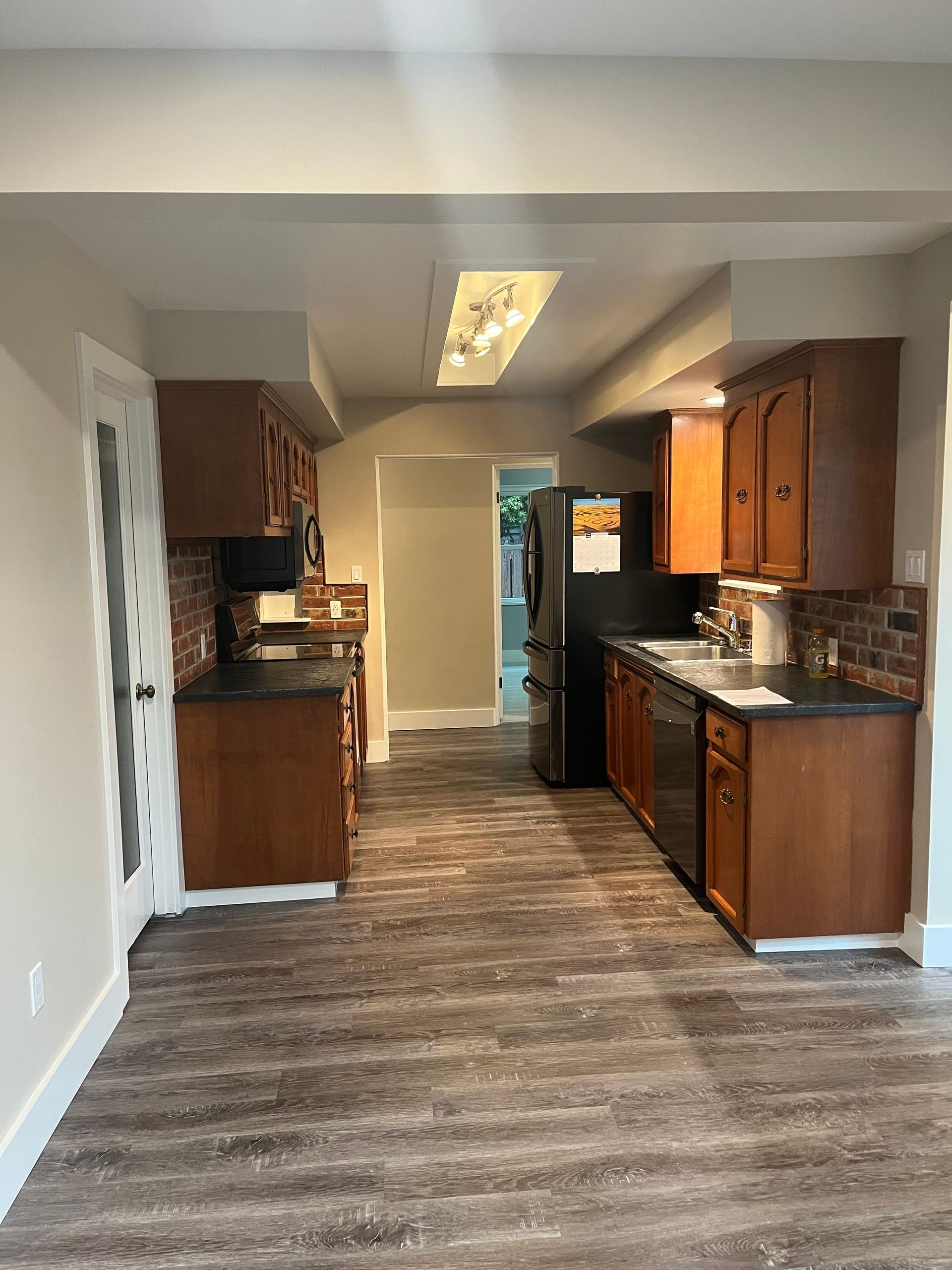 Empty kitchen with wood cabinets, dark countertops, and patterned flooring, viewed from the open living area