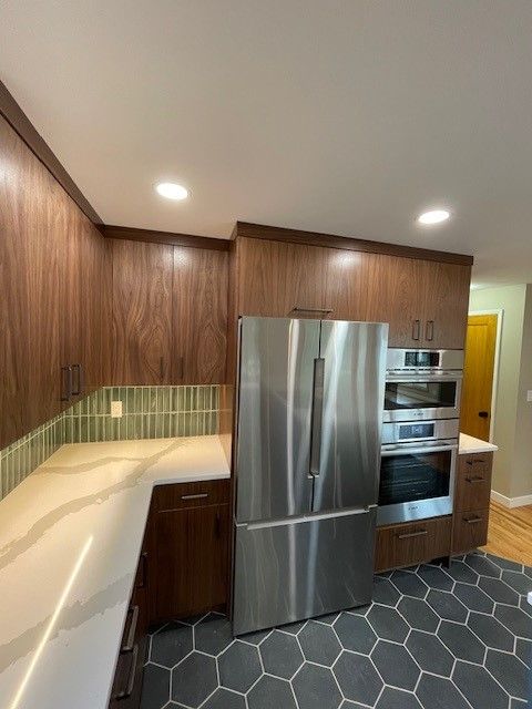 Modern kitchen with stainless steel refrigerator and oven, wood cabinets, white counters, and hex tile floor