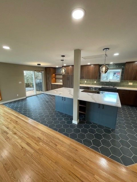 Modern kitchen with navy island, white countertops, wood floors, and hex tile flooring
