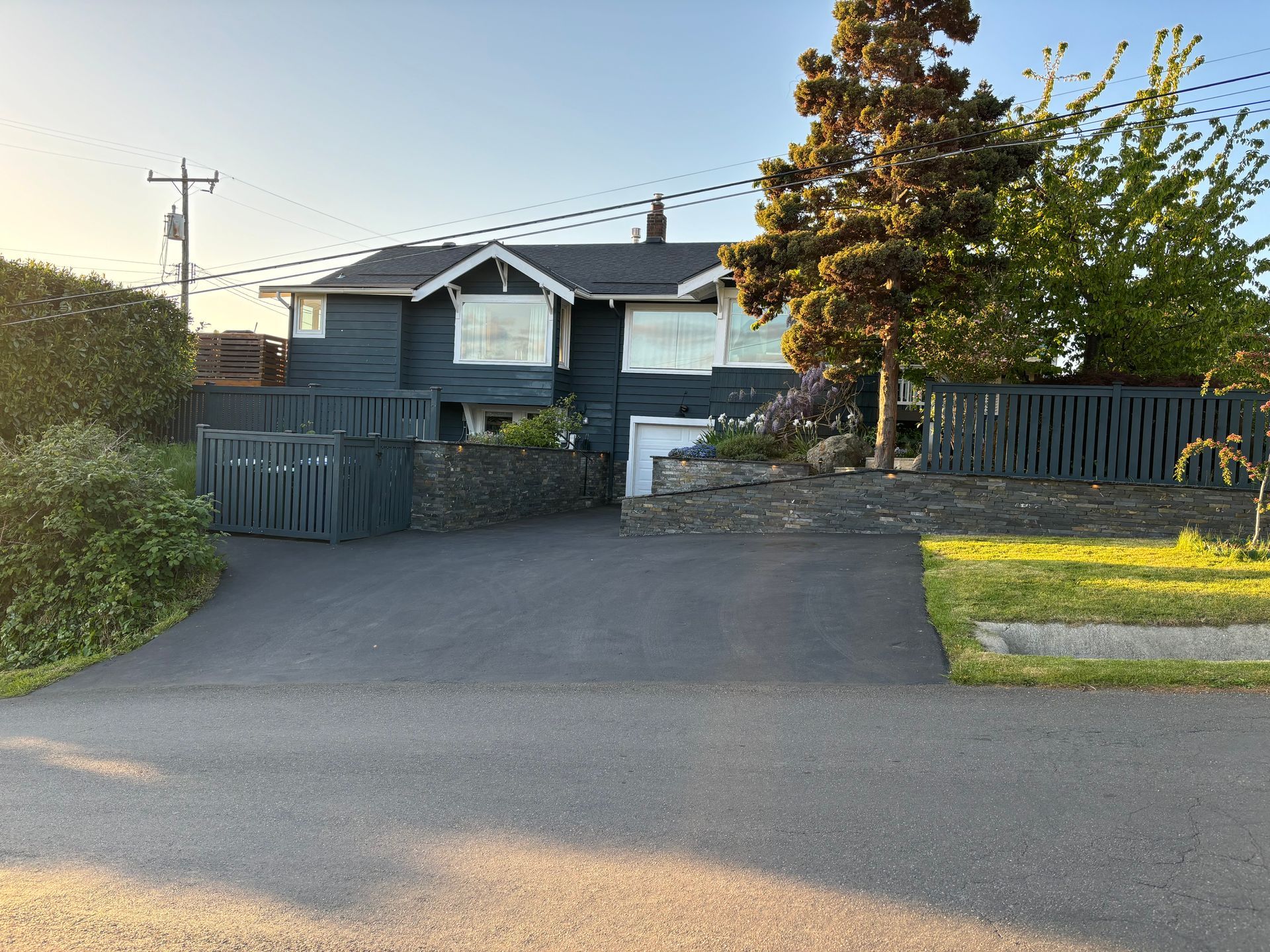 Suburban house with dark gray siding, driveway, and front fence under bright daylight