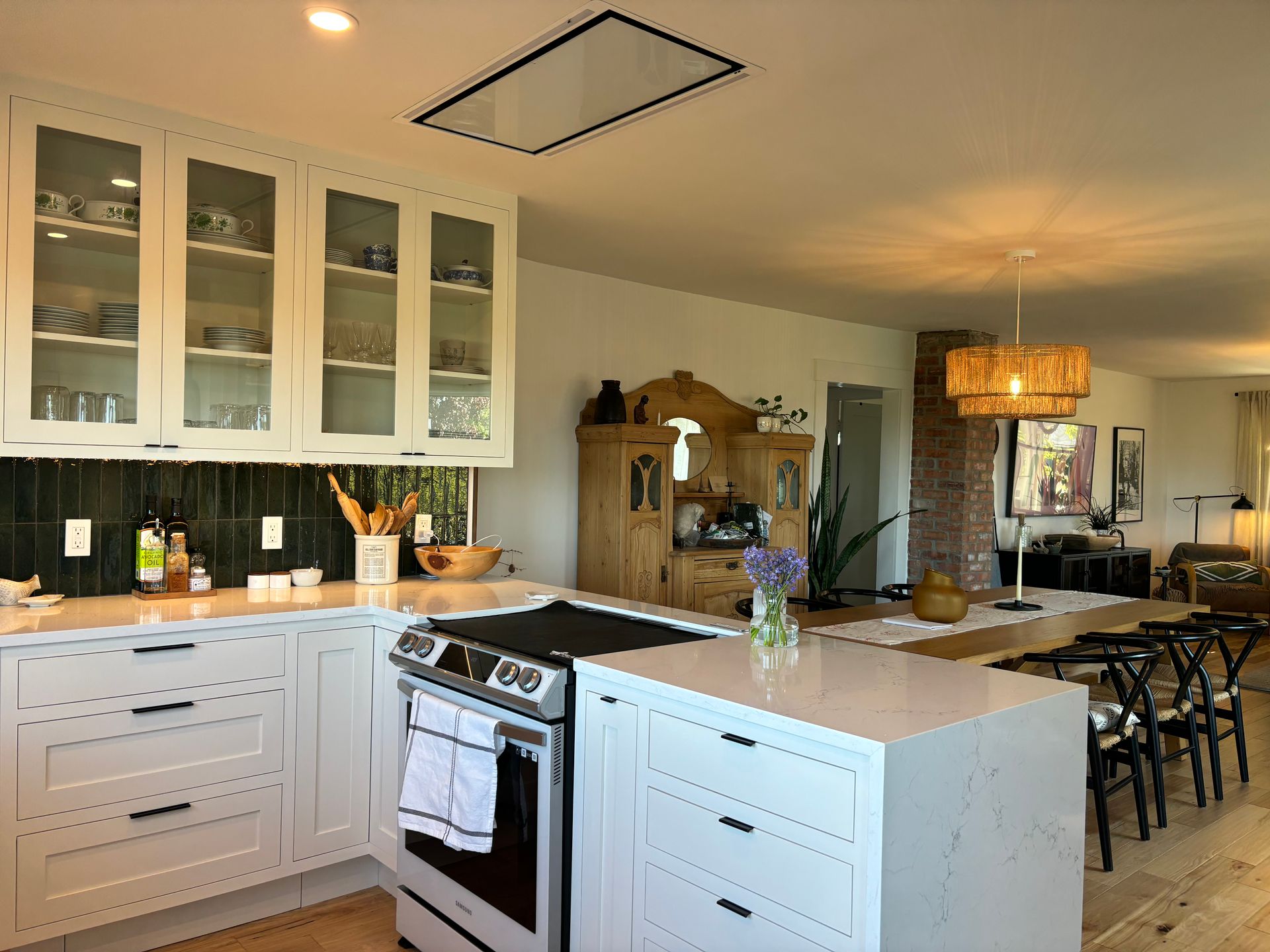 Modern white kitchen with island, glass cabinets, stove, and adjacent dining area