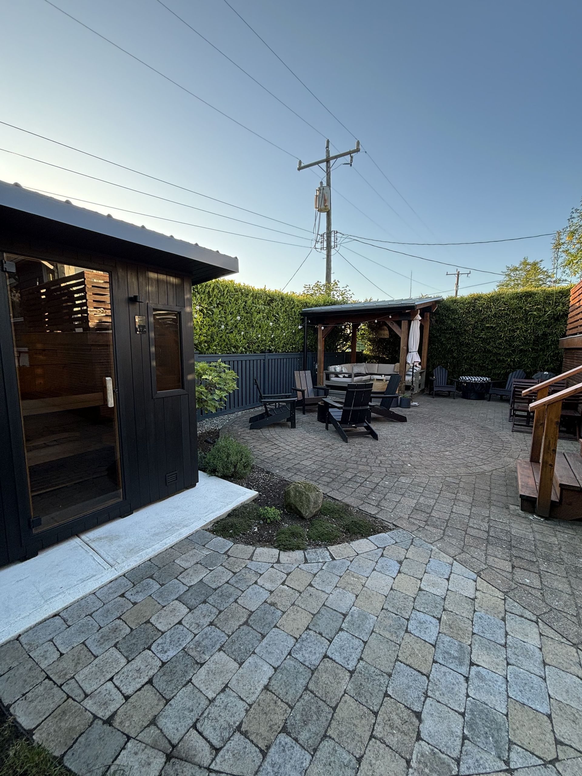 Backyard patio with pavers, outdoor seating, wooden shed, and garden vines under a clear sky