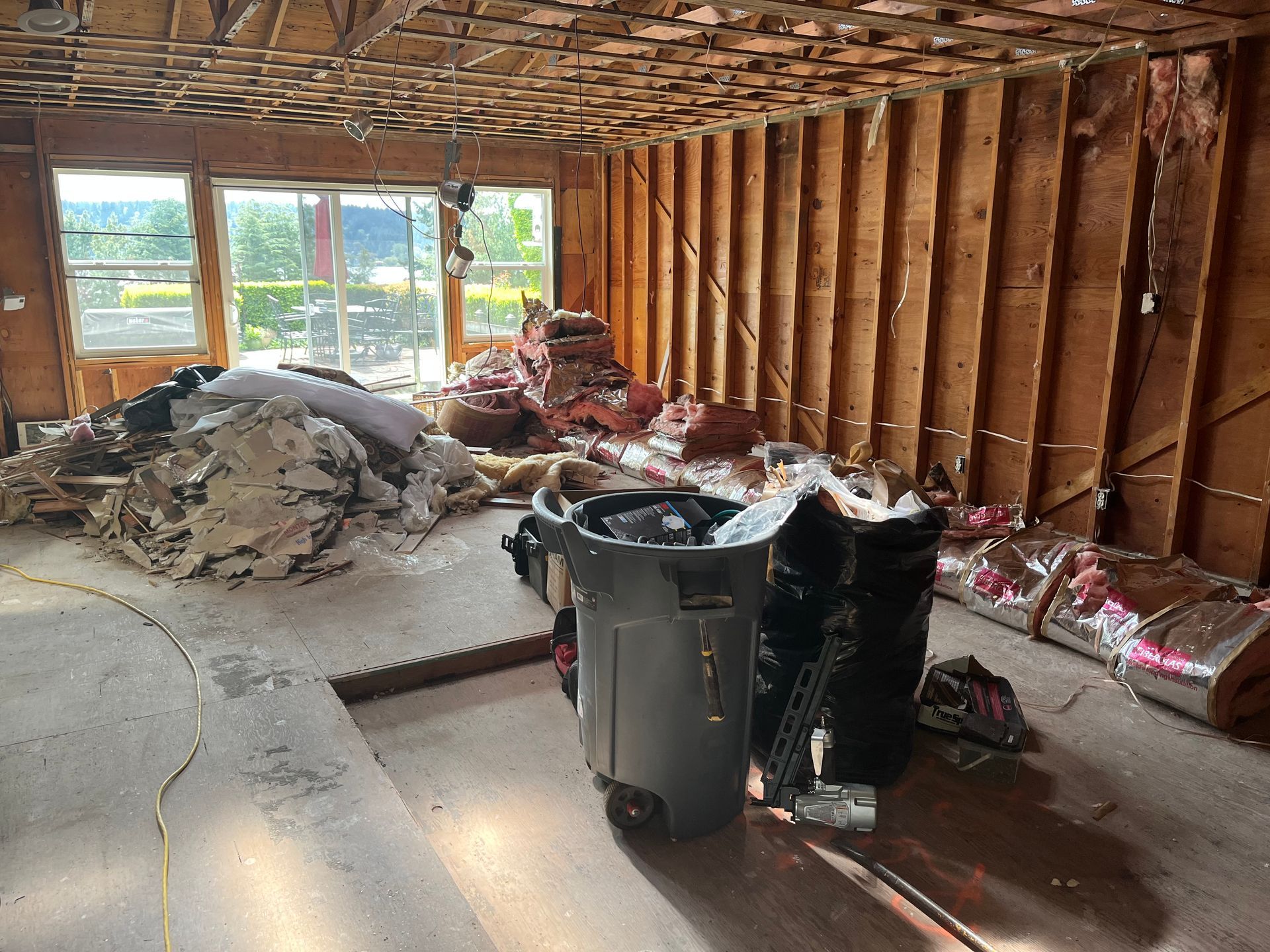 Unfinished room with exposed studs, piles of debris, and two trash bins near the center.