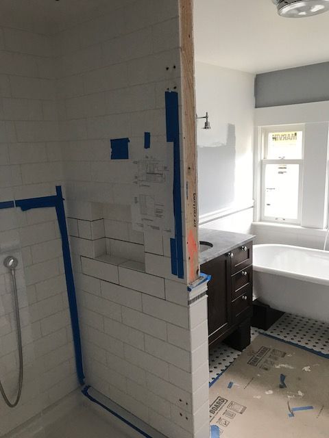 Bathroom under renovation with tiled shower wall, blue tape, and vanity beside a toilet.
