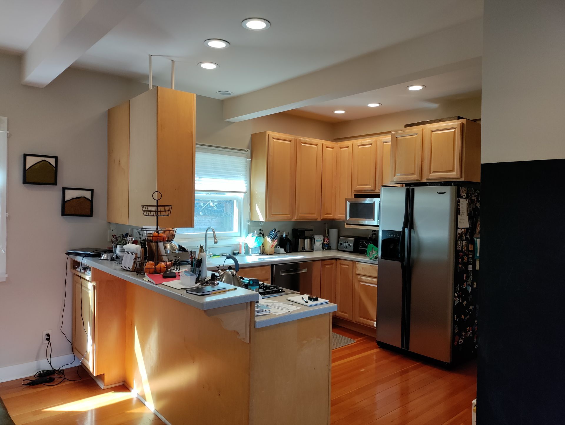Bright kitchen with wooden cabinets, stainless fridge, island counter, and sunlight on hardwood floor