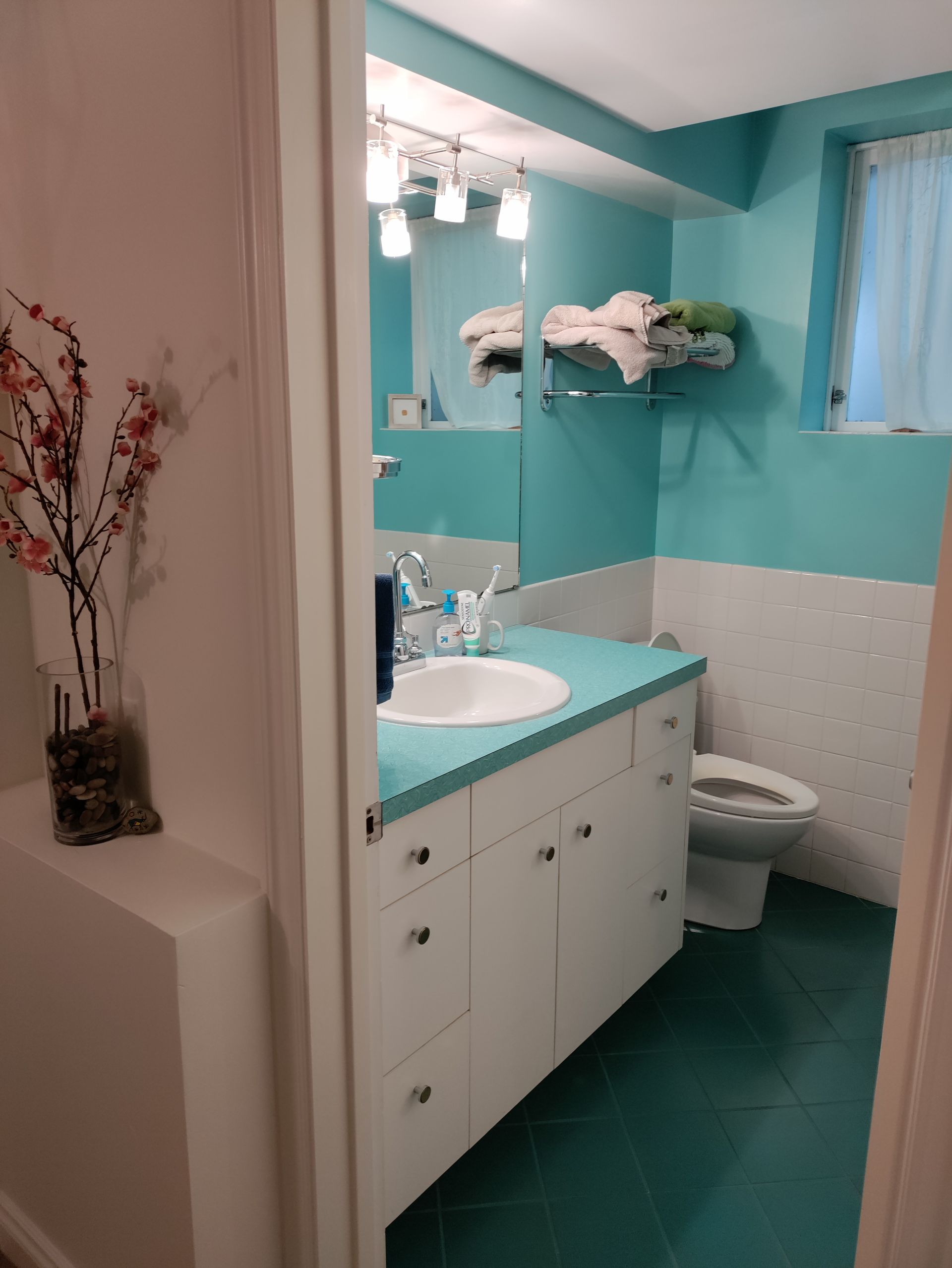 Bright turquoise bathroom with white vanity, toilet, and frosted window.