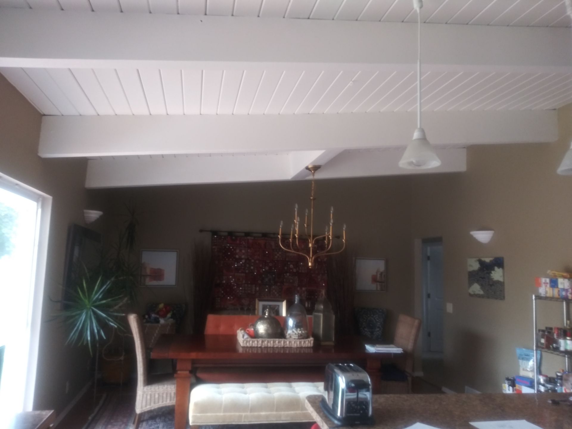 Living room with high white ceiling, chandelier, wooden table, sofa, and large window on the left
