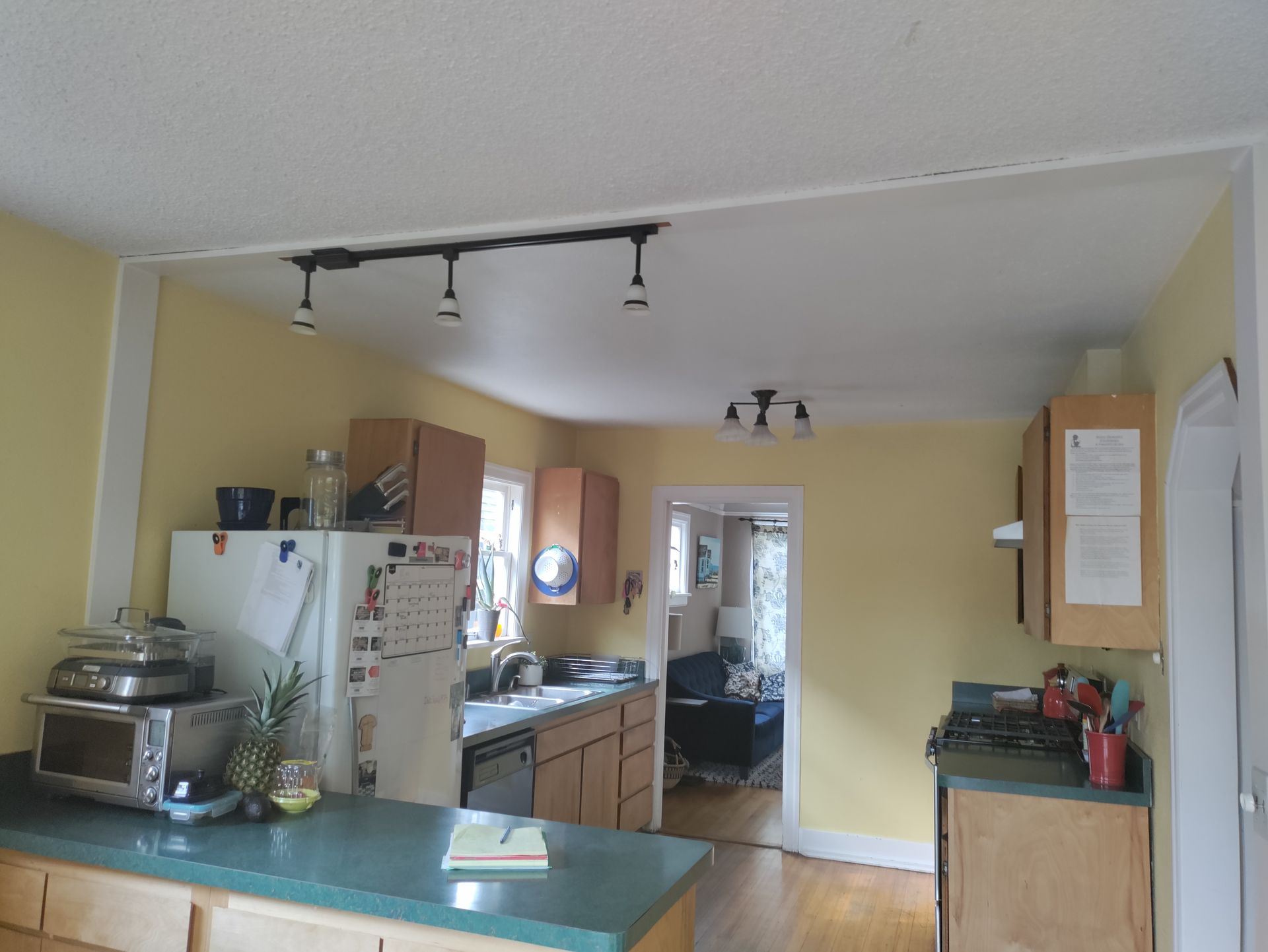 Small kitchen with yellow walls, white cabinets, and a green countertop, viewed from the dining area.