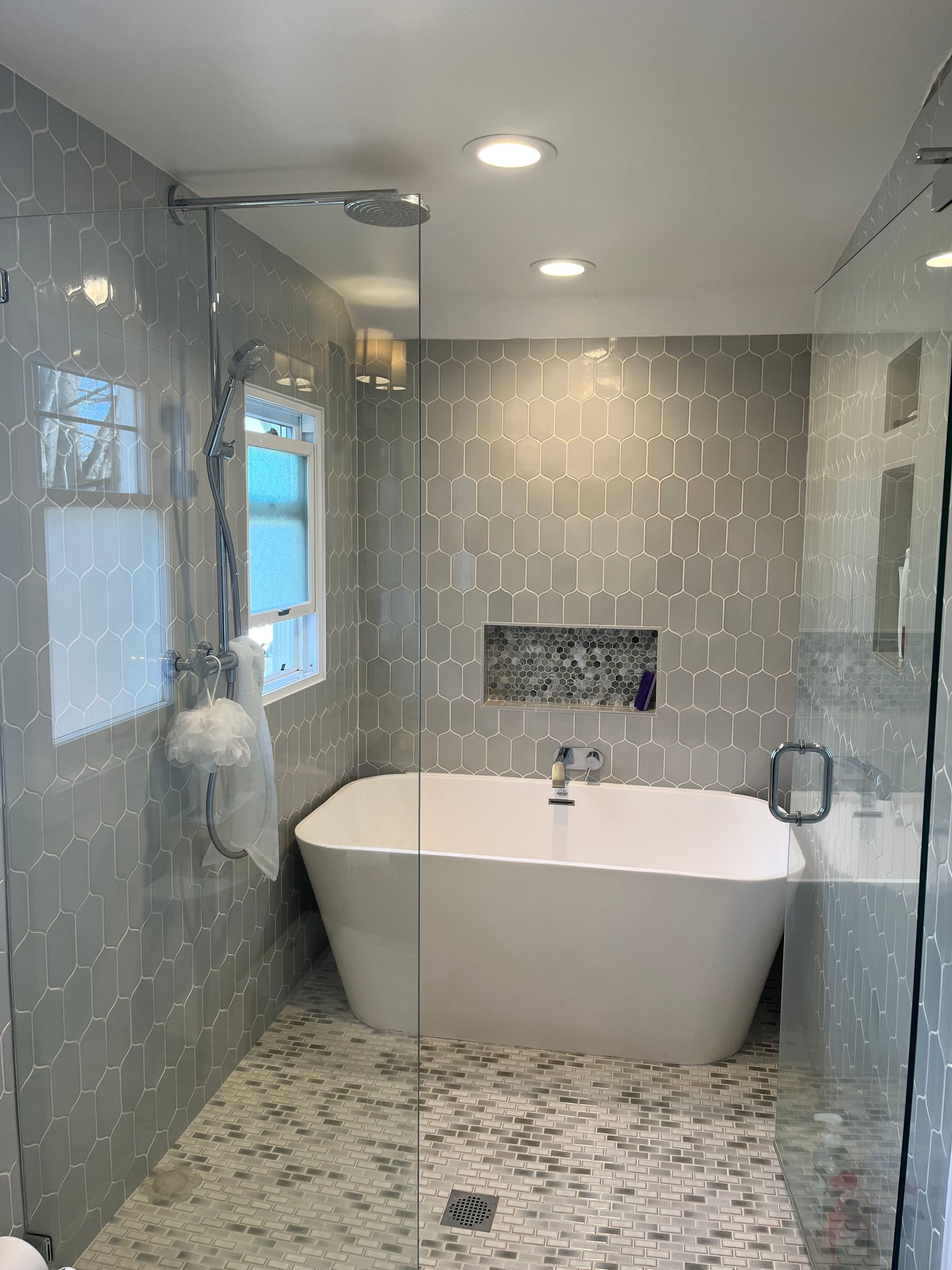Modern bathroom with freestanding tub, tiled shower walls, glass enclosure, and pebble mosaic floor.