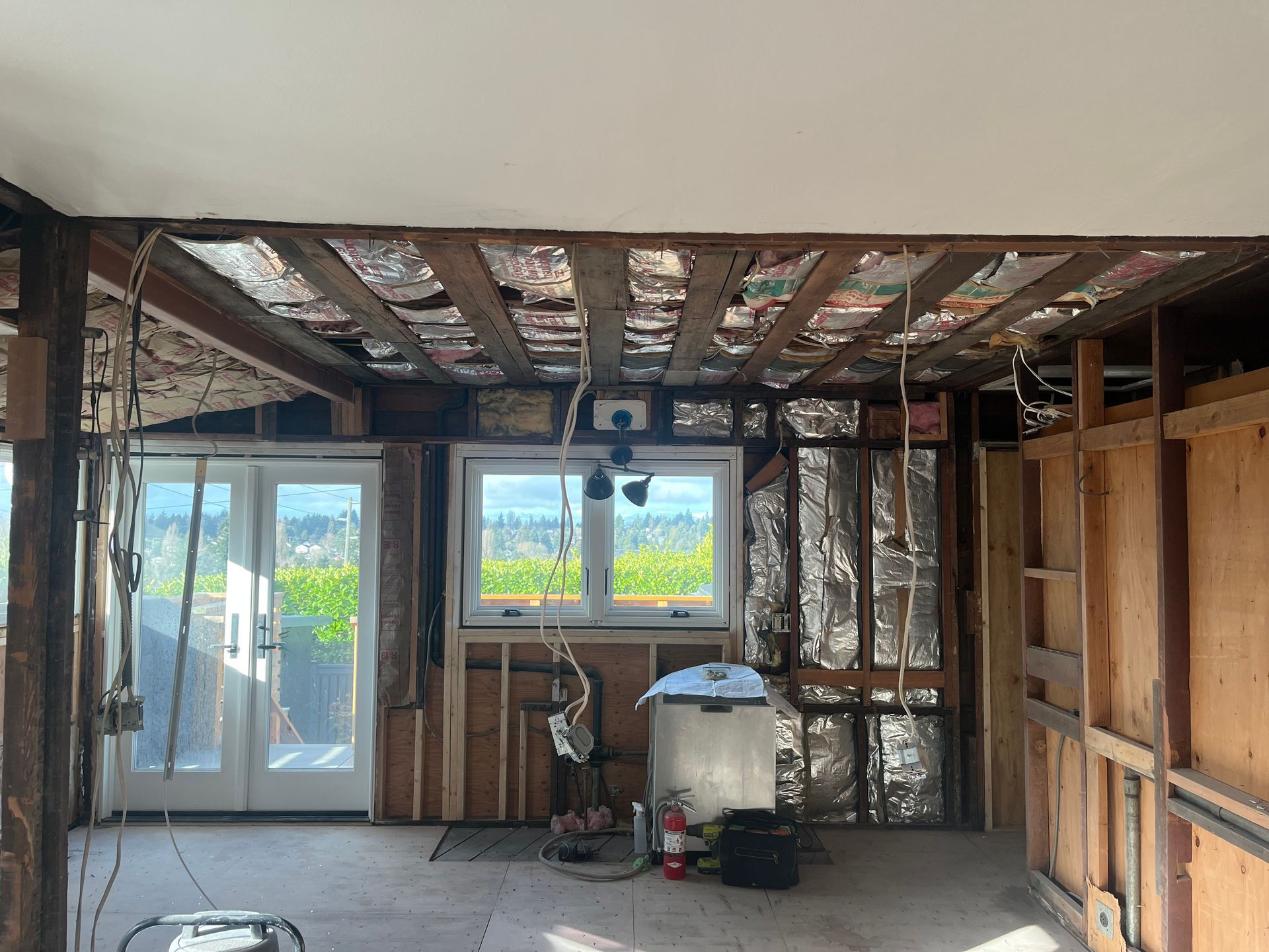 Interior of a room under renovation with exposed studs, unfinished ceiling, and a window and sliding door.