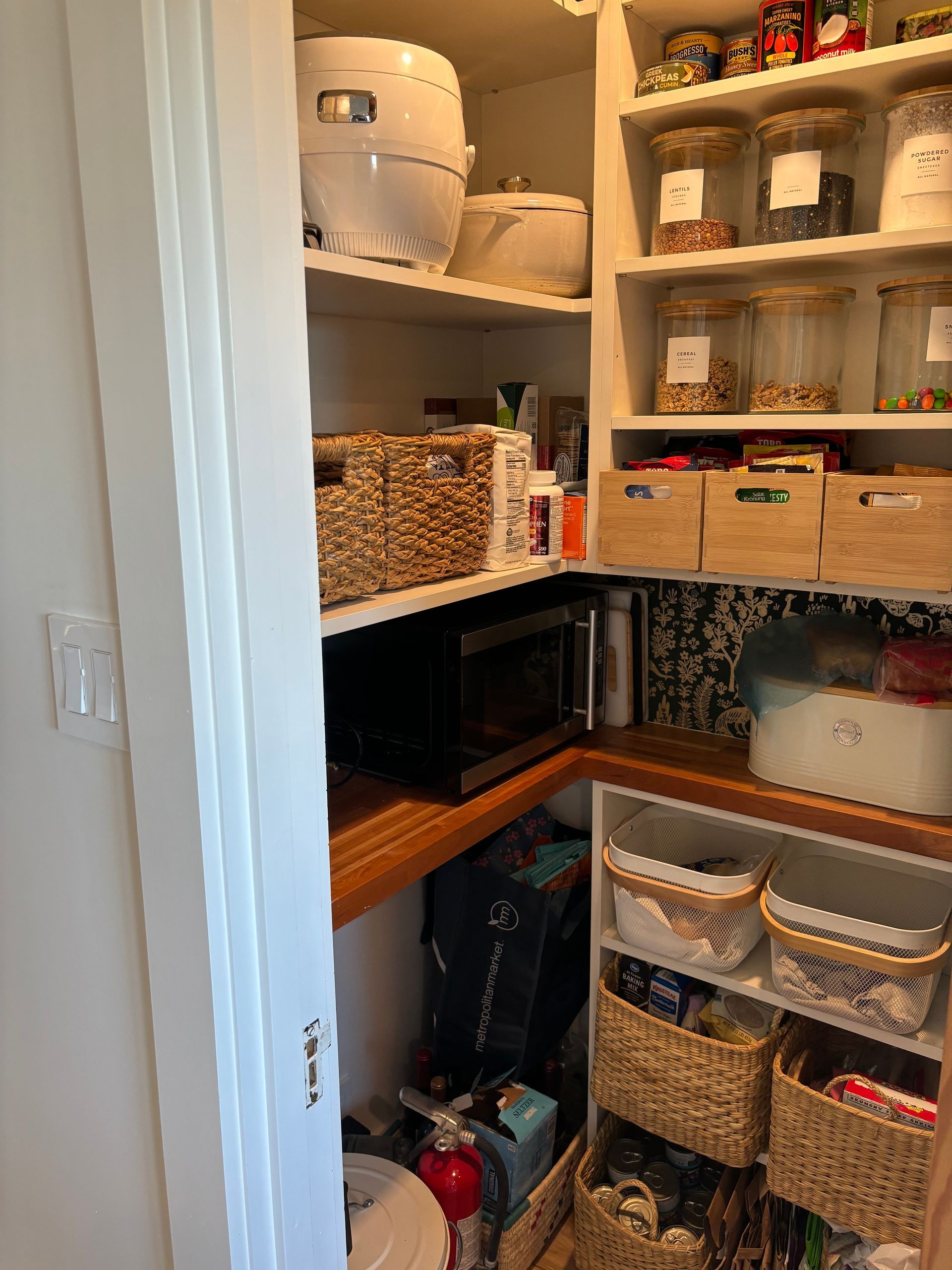 Open pantry closet with shelves, baskets, bins, and kitchen appliances organized inside.