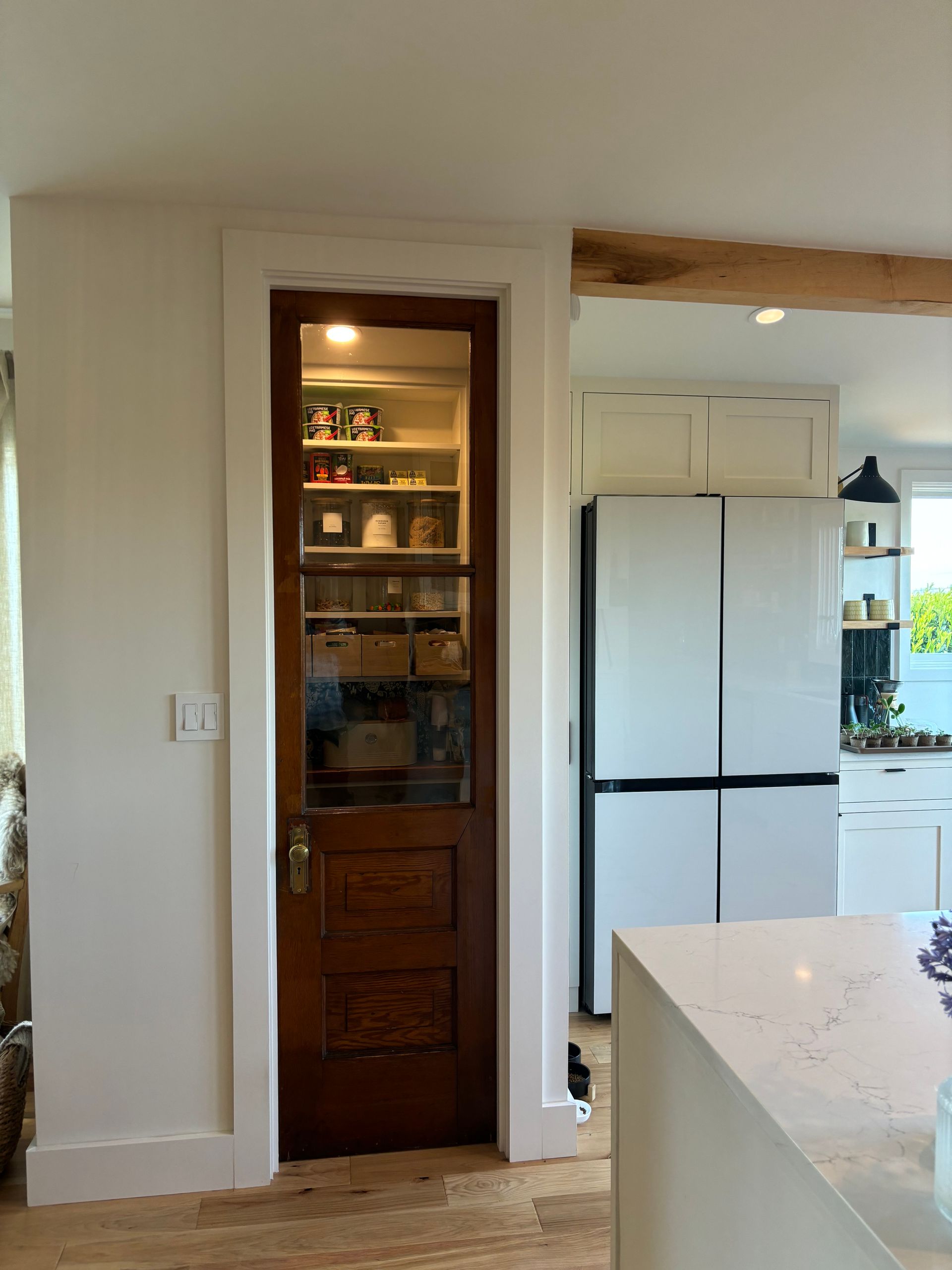 Kitchen interior with white cabinets, a stainless refrigerator, and a narrow pantry doorway.