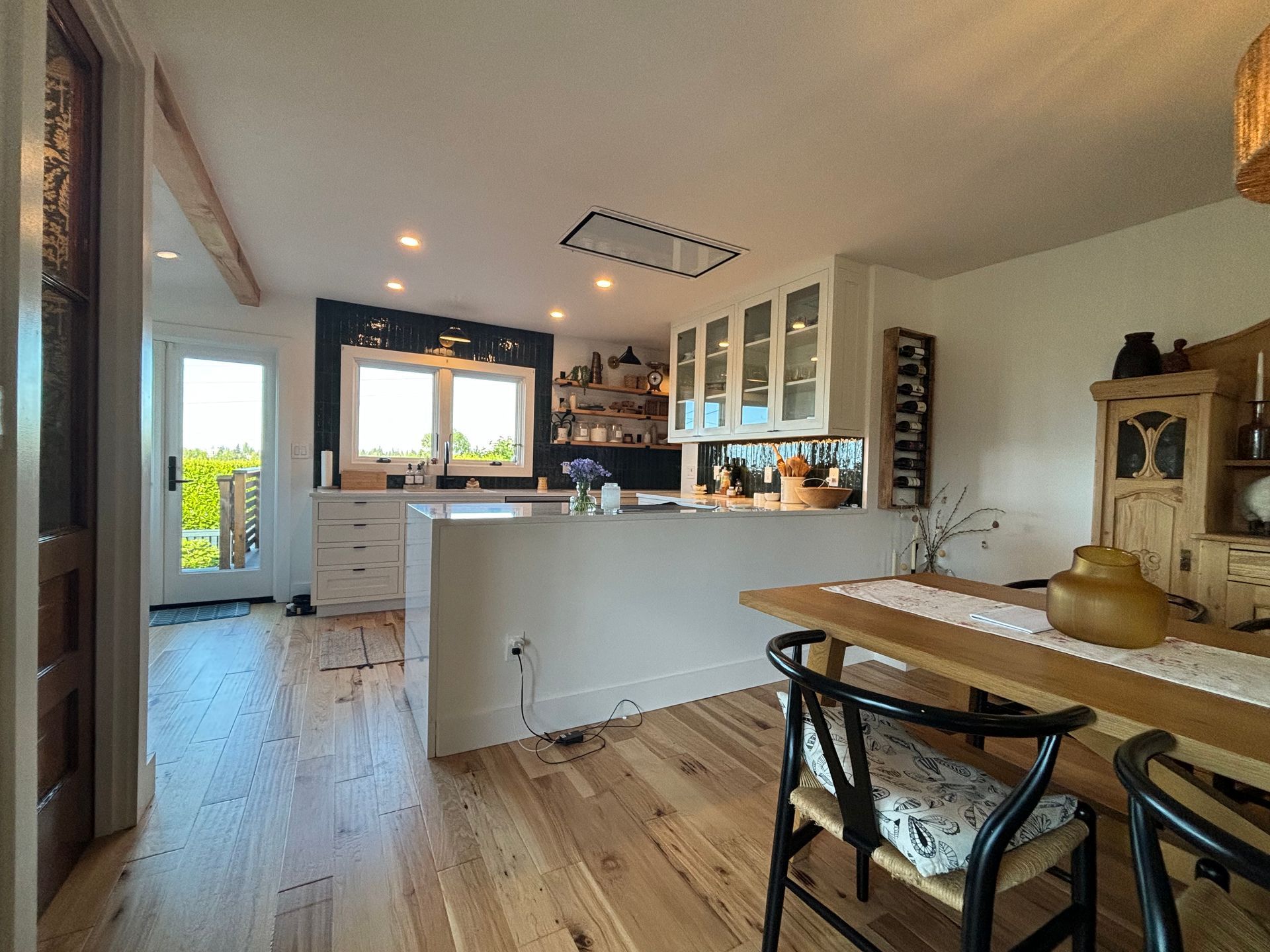 Bright modern kitchen and dining area with wood floors, white island, and large windows