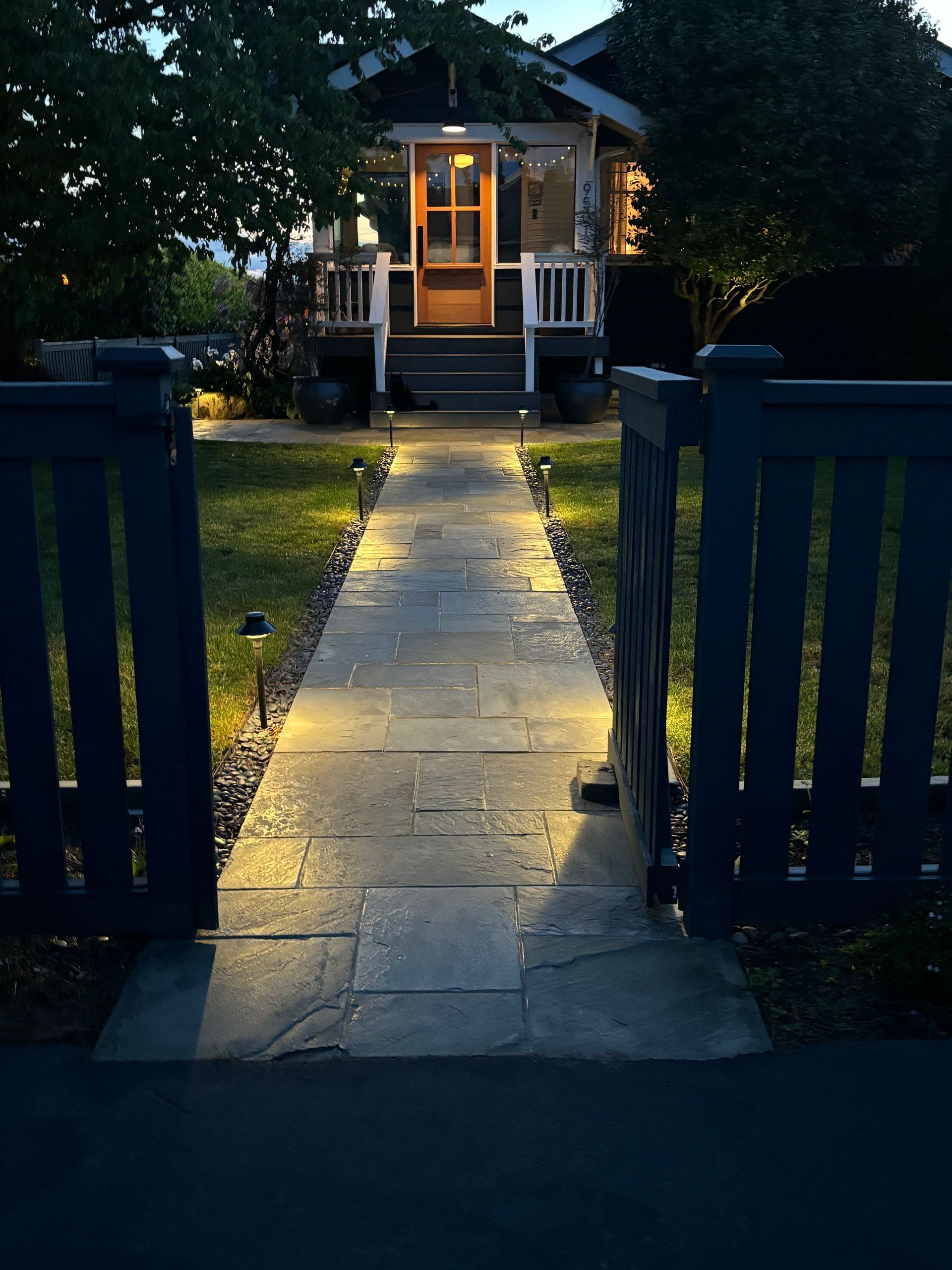 Front gate opens to a lit stone path leading to a warmly lit house at dusk