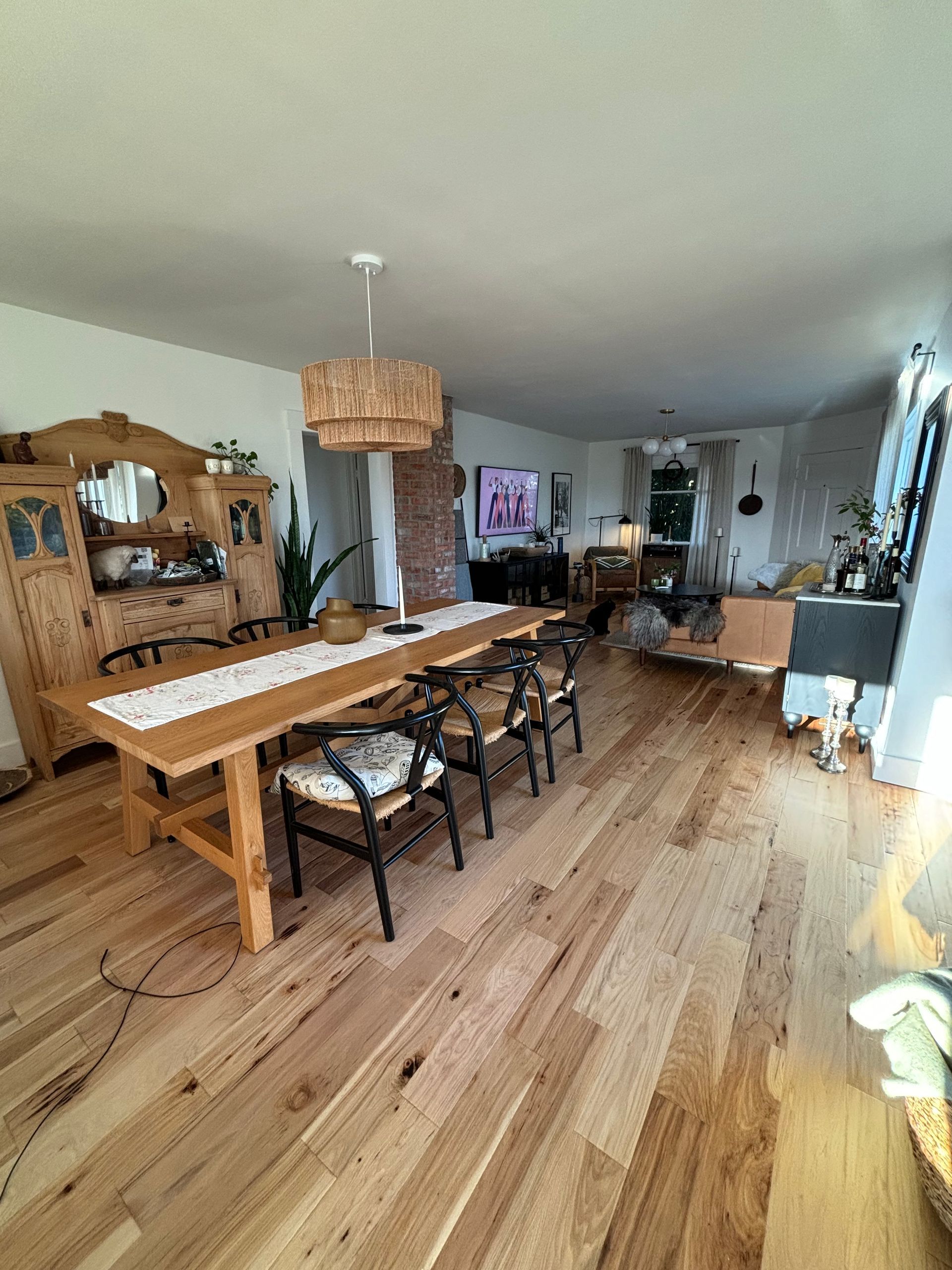 Bright dining room and living area with a long wooden table, woven pendant light, and wood floors