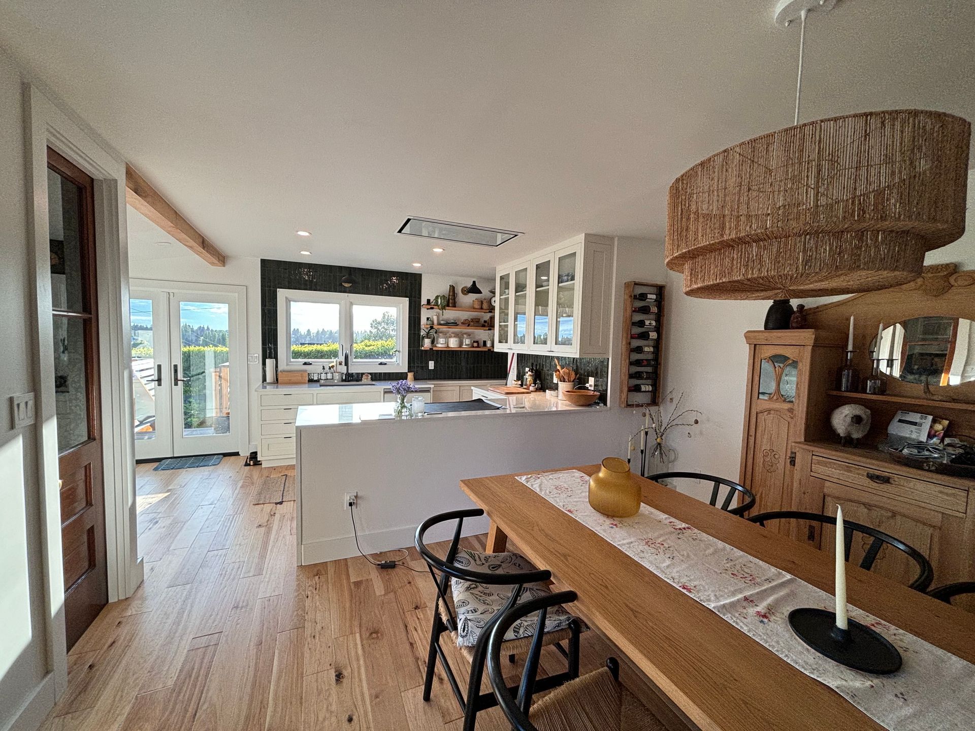 Bright open kitchen and dining area with white cabinets, wood floors, and a large woven pendant light